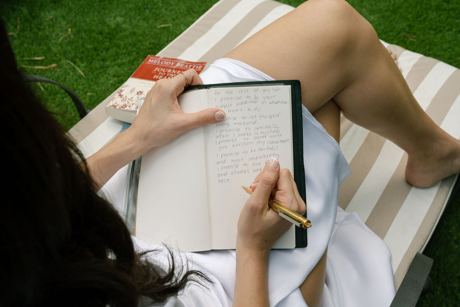 Person writing in a journal while relaxing on a striped blanket outdoors.