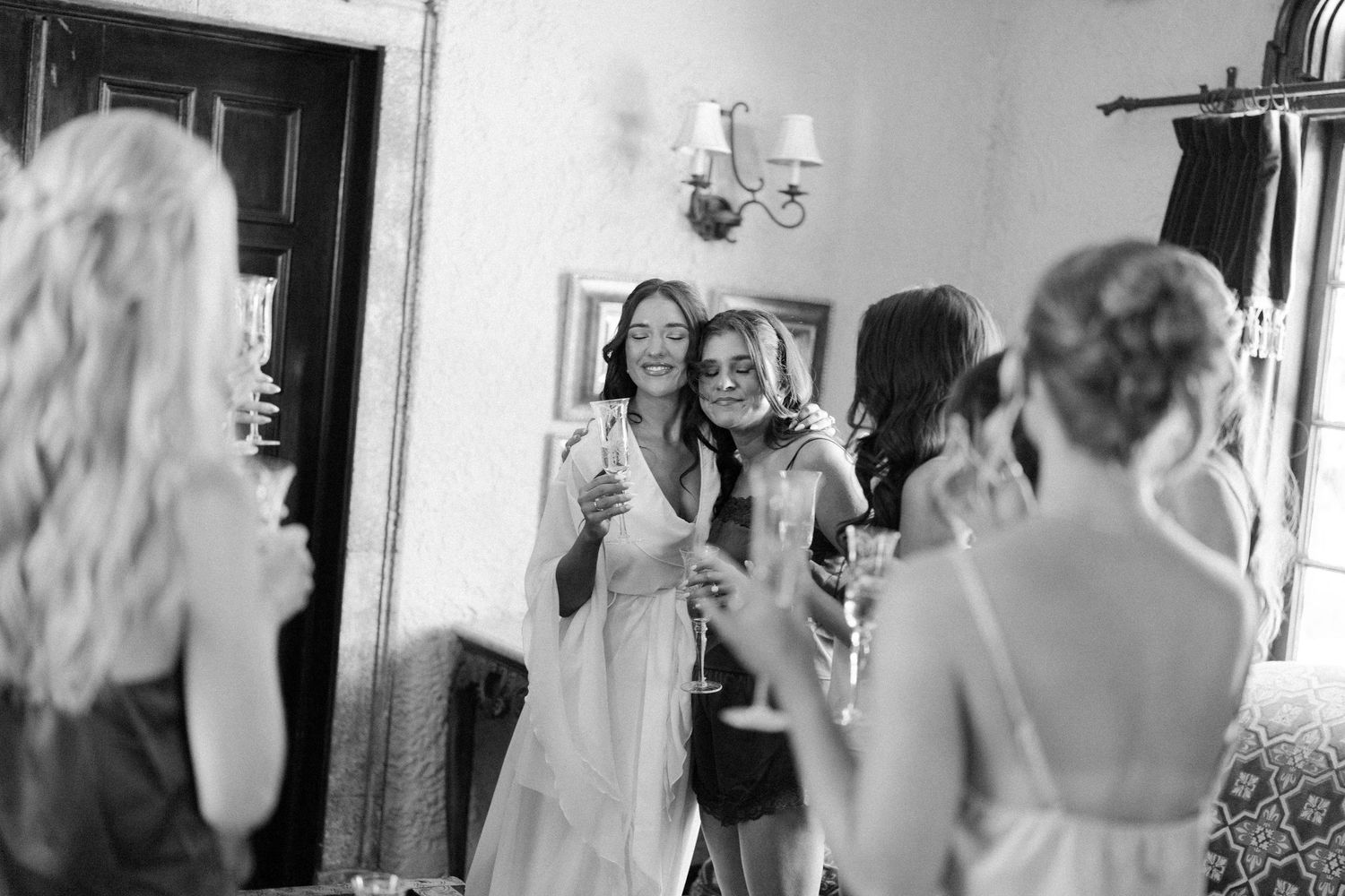 Black and white photo of bridesmaids celebrating with champagne glasses reflected in a mirror.