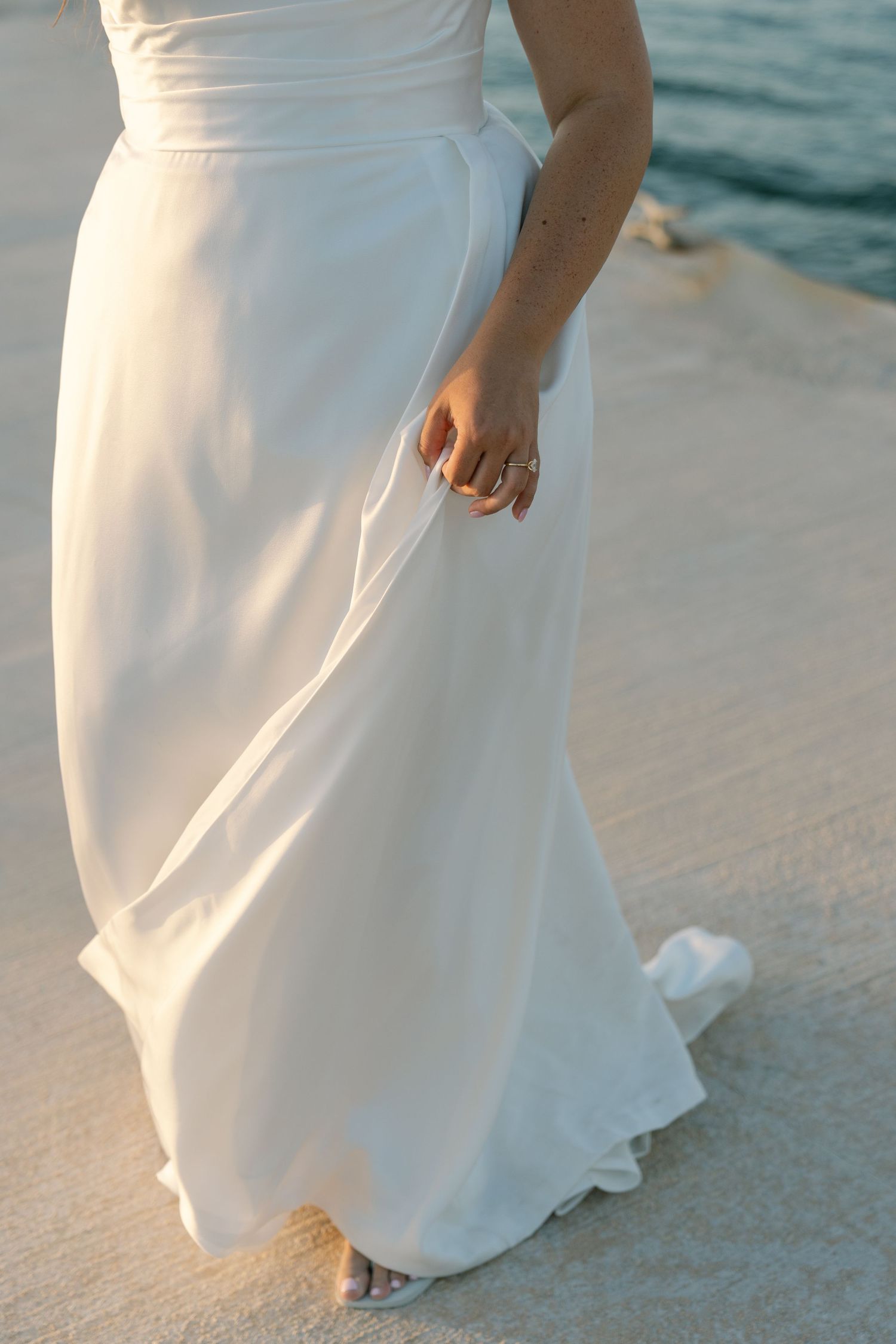 A close-up view of a woman's dress as she walks on a beach with the ocean in the background.