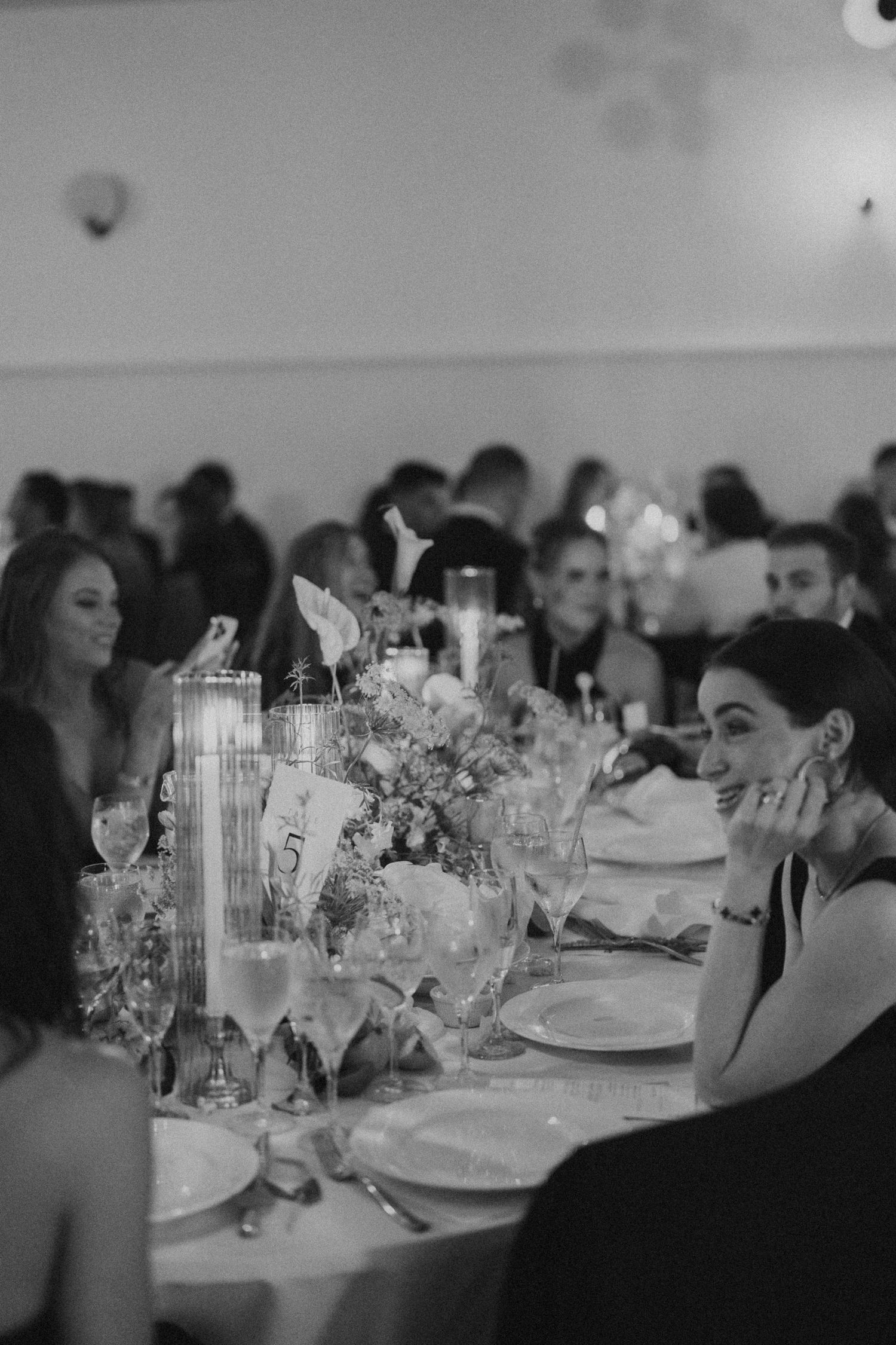 Wedding reception table settings with elegant floral arrangements and glassware in dim lighting.
