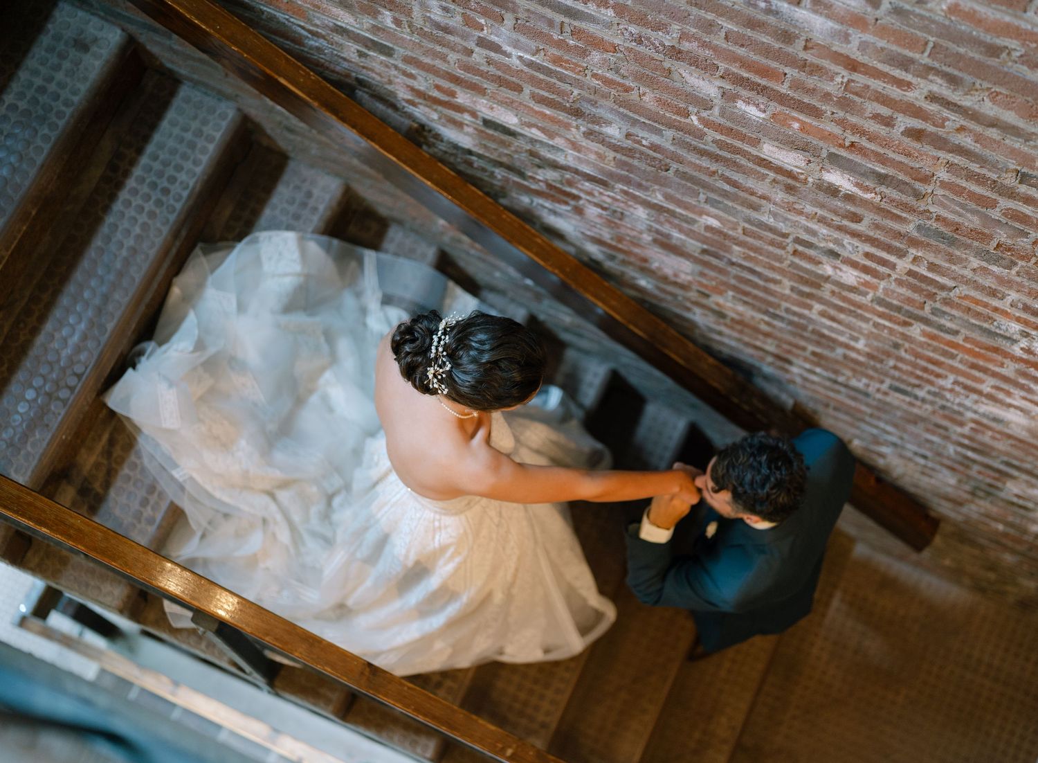 A person in an elegant wedding gown walks down an aisle with exposed brick walls in a rustic indoor venue.