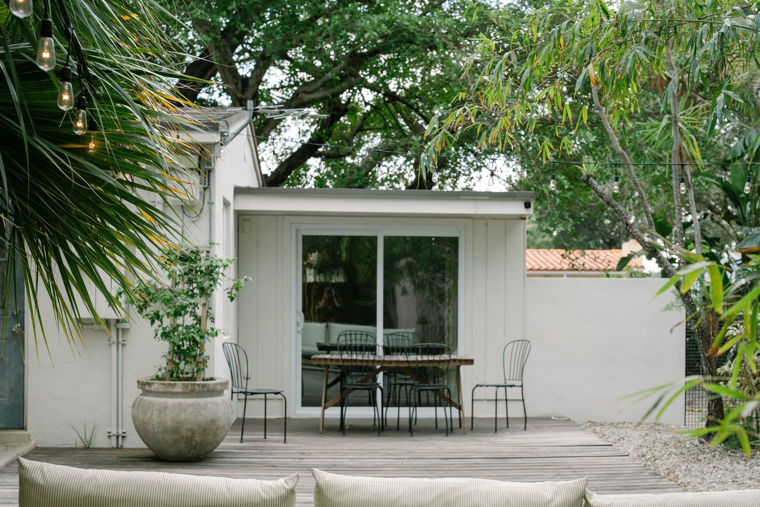 Tropical garden patio area with white walls, wooden beams, and outdoor furniture creating a peaceful seating space.