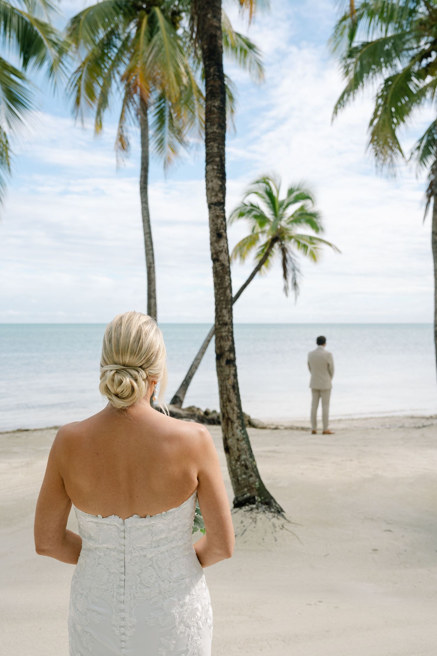 A tropical beach wedding first look moment with palm trees and ocean view.