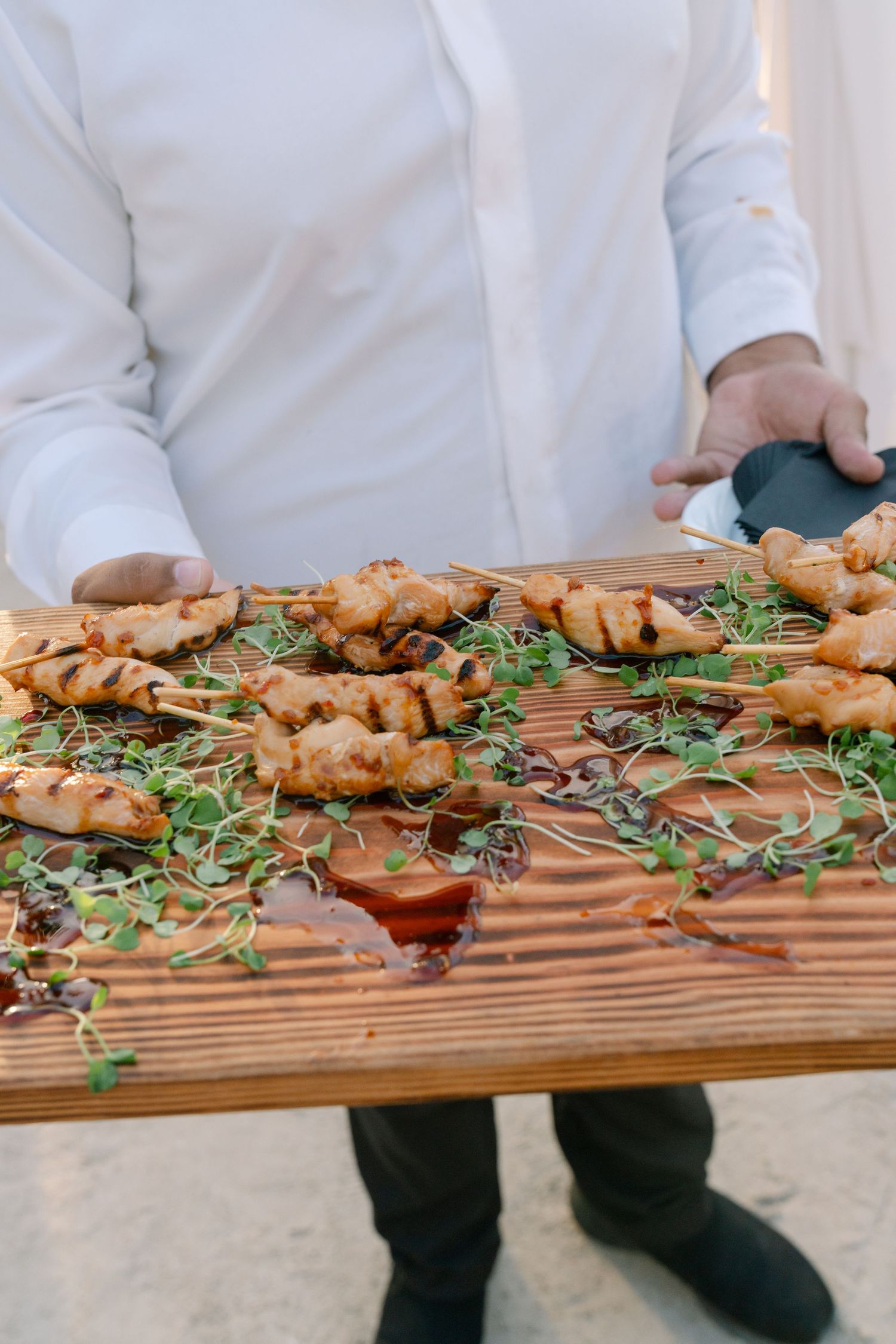 Catering display of grilled skewers garnished with fresh herbs on wooden serving board.