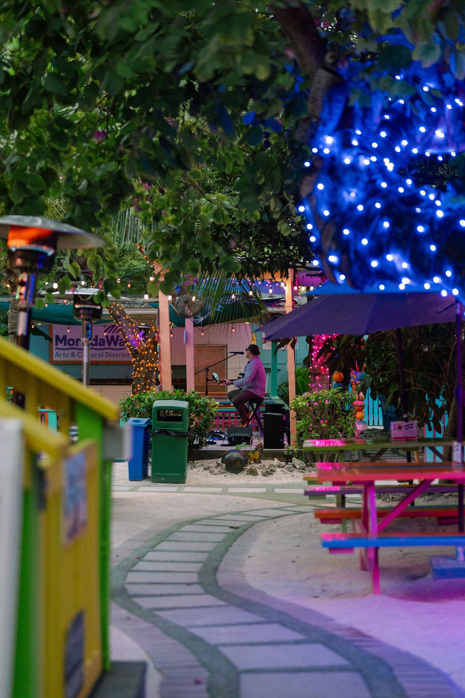 Colorful outdoor seating area illuminated by blue string lights creating a magical nighttime atmosphere in a garden setting.