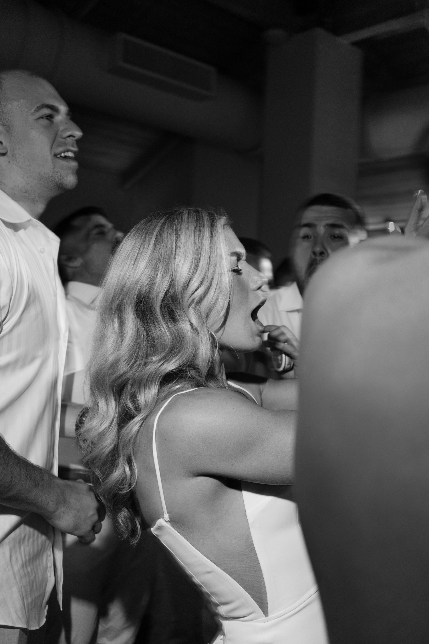 Black and white photo of wedding guests dancing and celebrating at a lively reception party.
