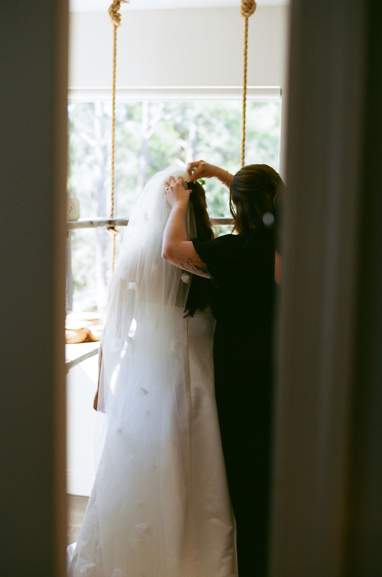 A bride and groom share an intimate dance in a sunlit room with white curtains and columns.