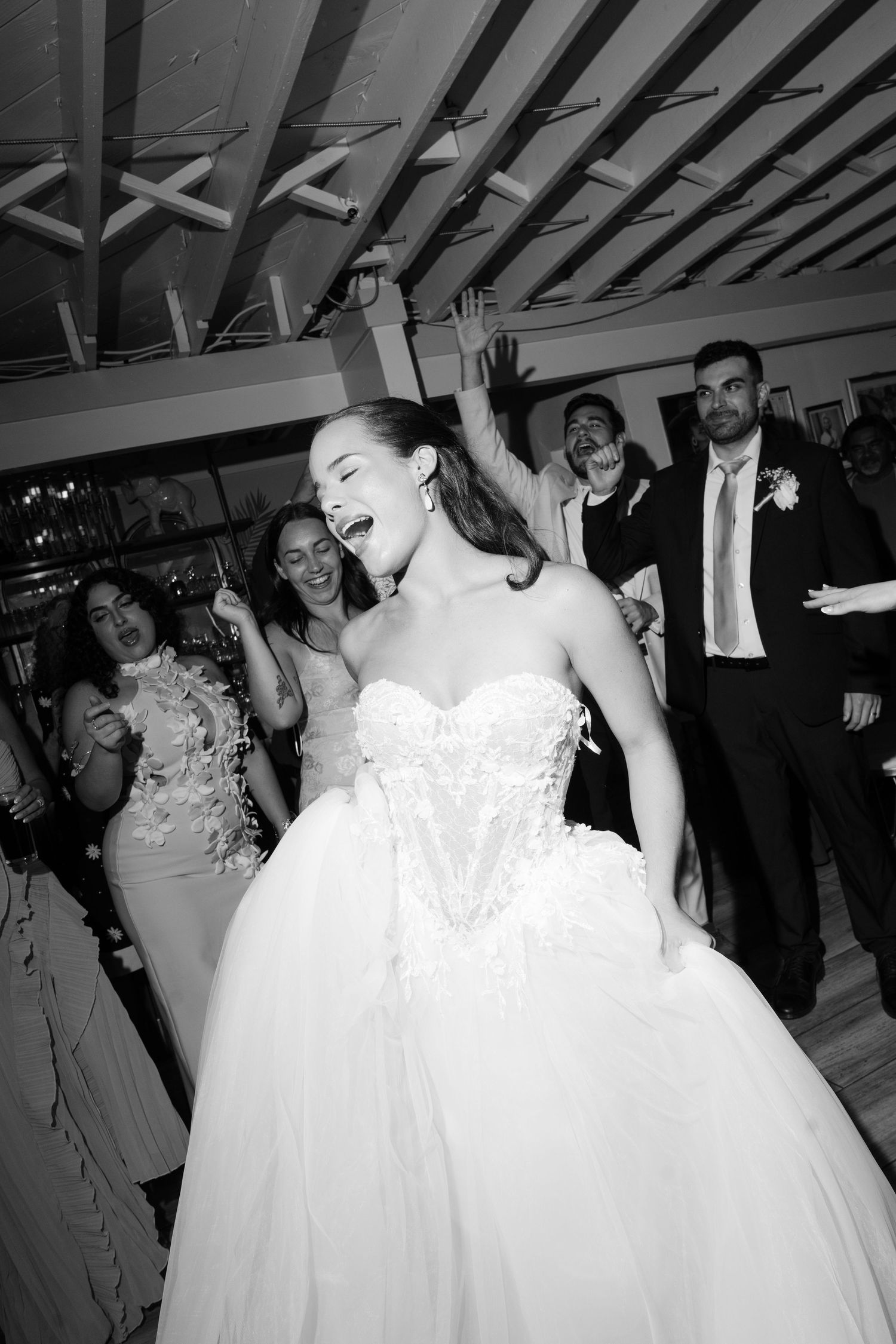 Radiant bride dancing joyfully in lace ballgown surrounded by celebrating wedding guests on dance floor.
