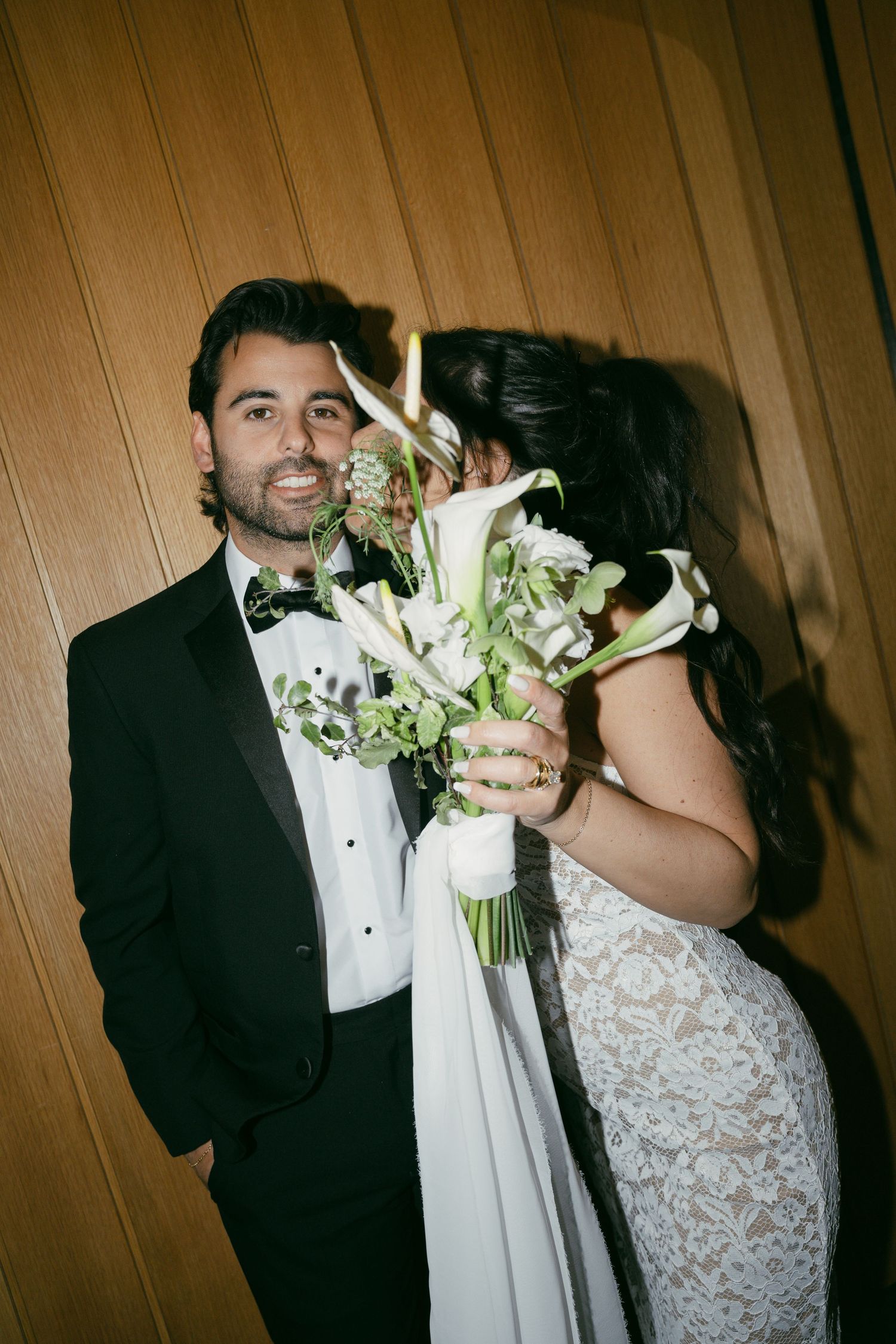 A series of wedding photos showing a couple with white flowers sharing intimate moments against a wooden wall.