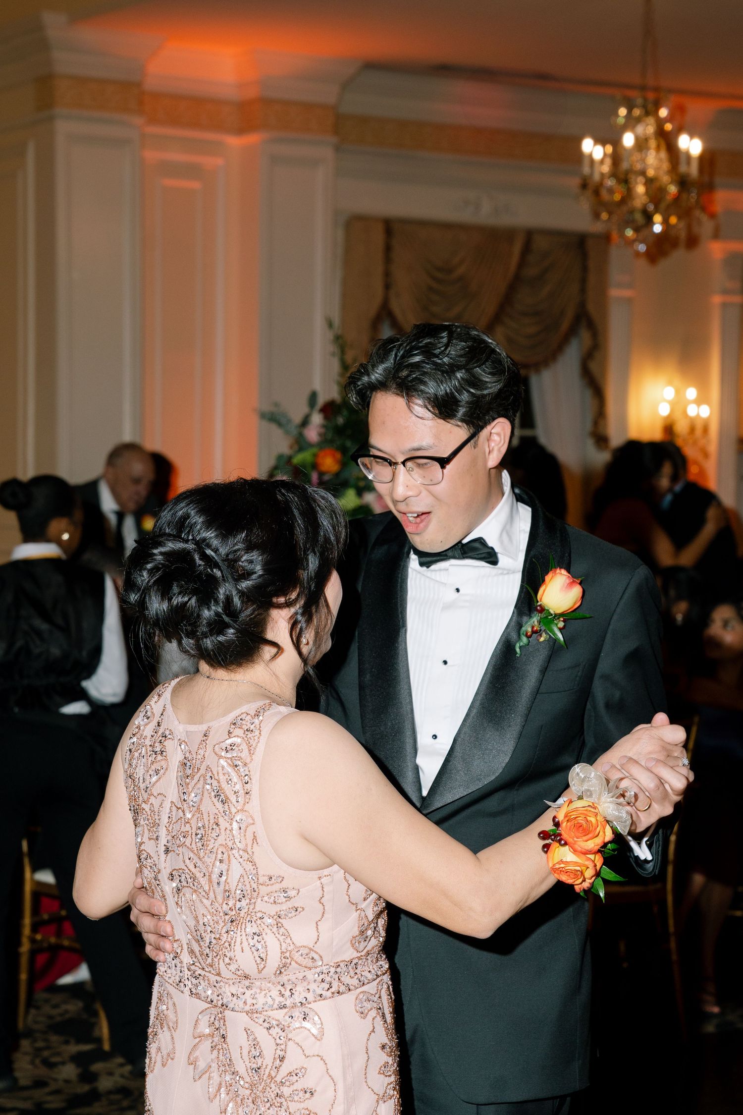 Couples dancing at formal wedding reception in elegant ballroom with warm lighting.