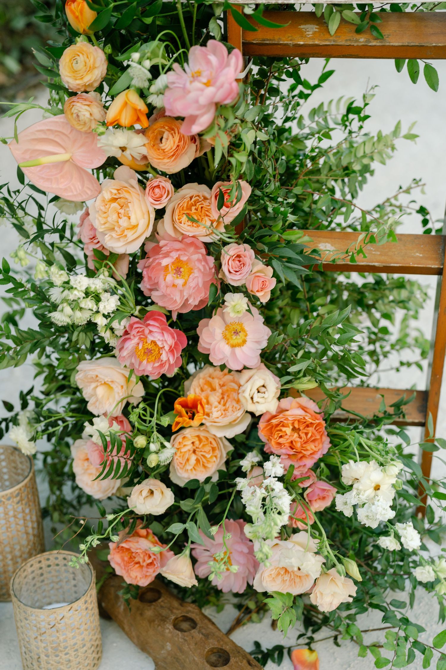Lush floral arrangement featuring peach and pink garden roses with delicate greenery against wooden ladder shelves.