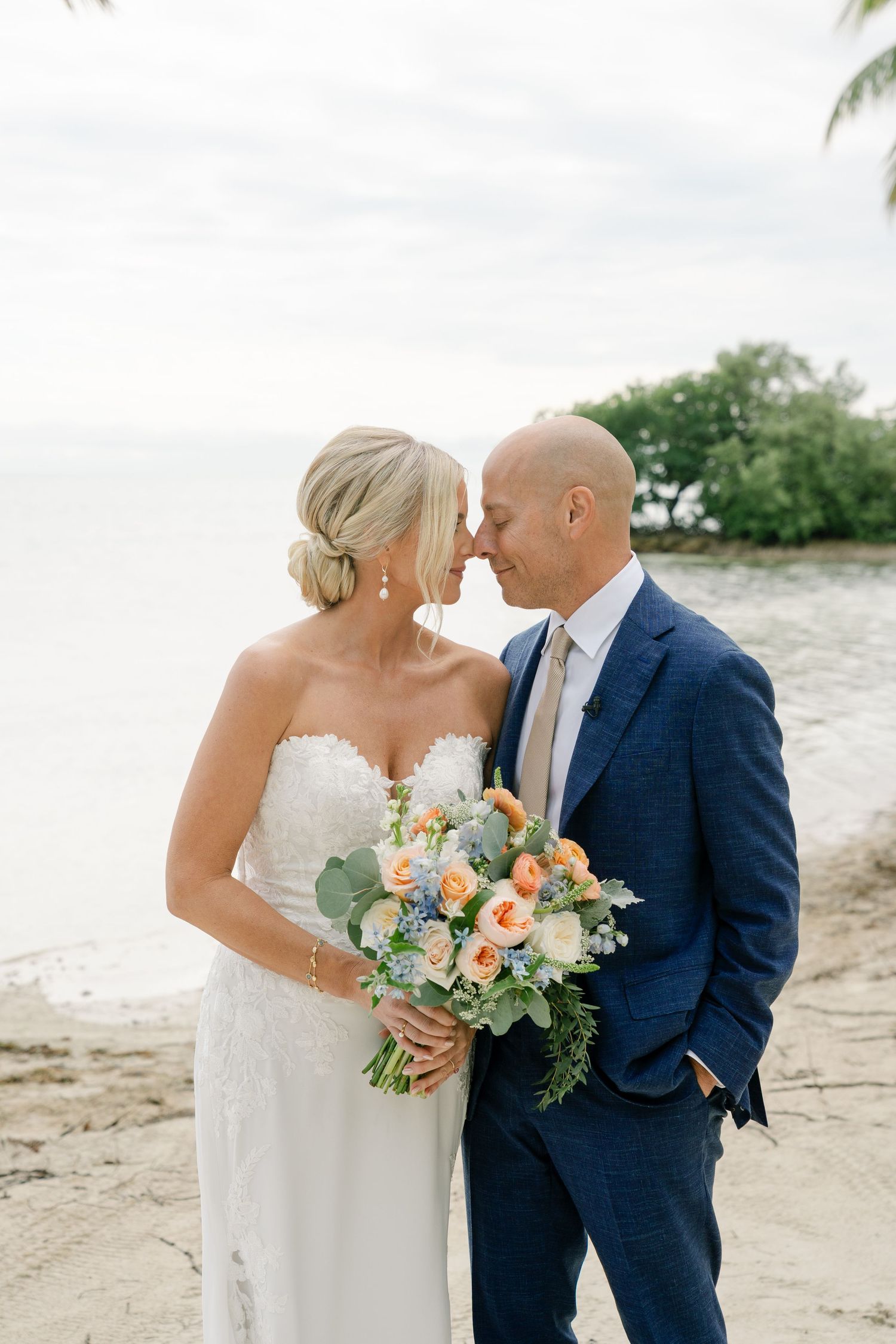 Romantic beach wedding moment with bridal bouquet featuring peach and white flowers.