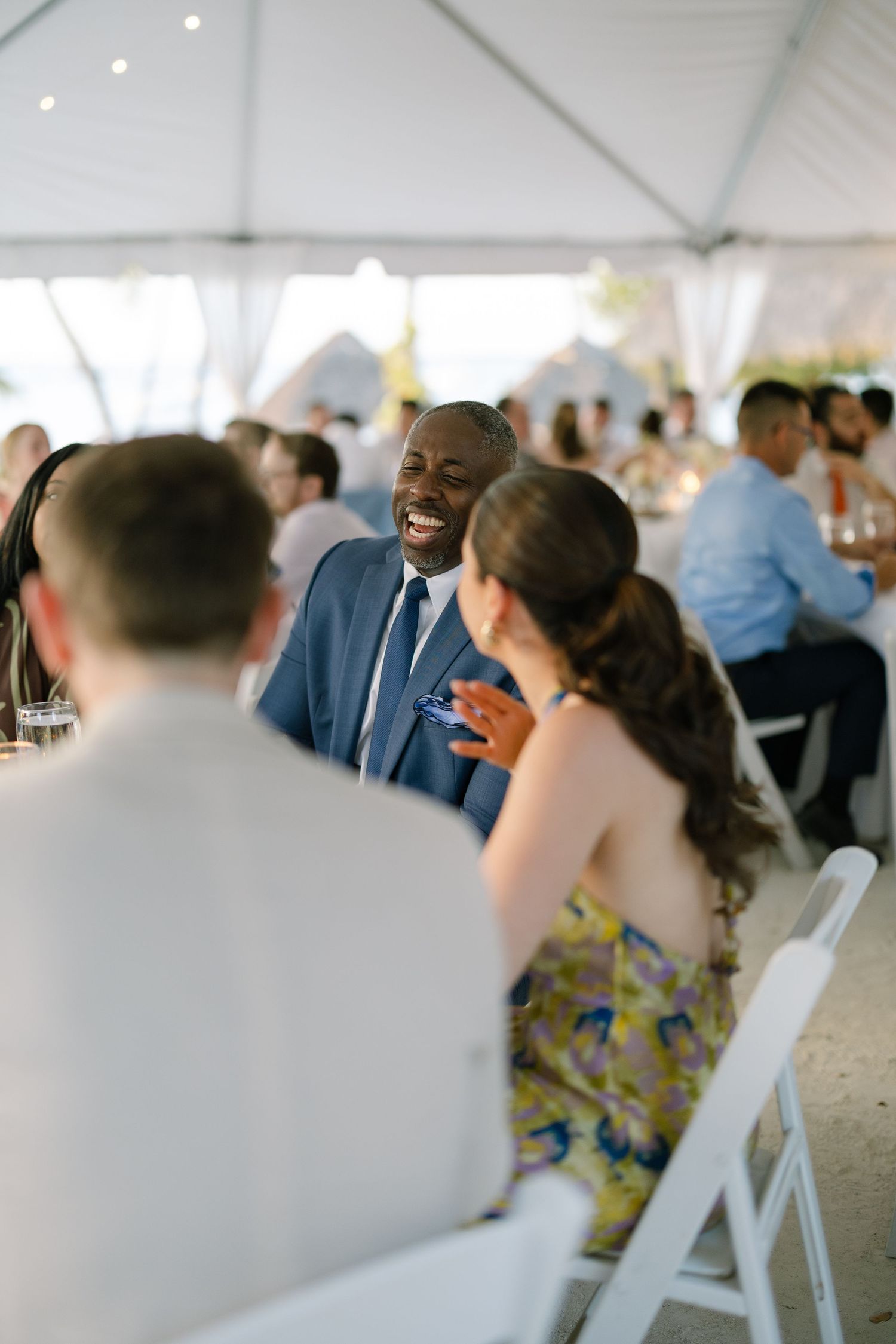 A man in a suit speaks to a woman at a table during an event or celebration.