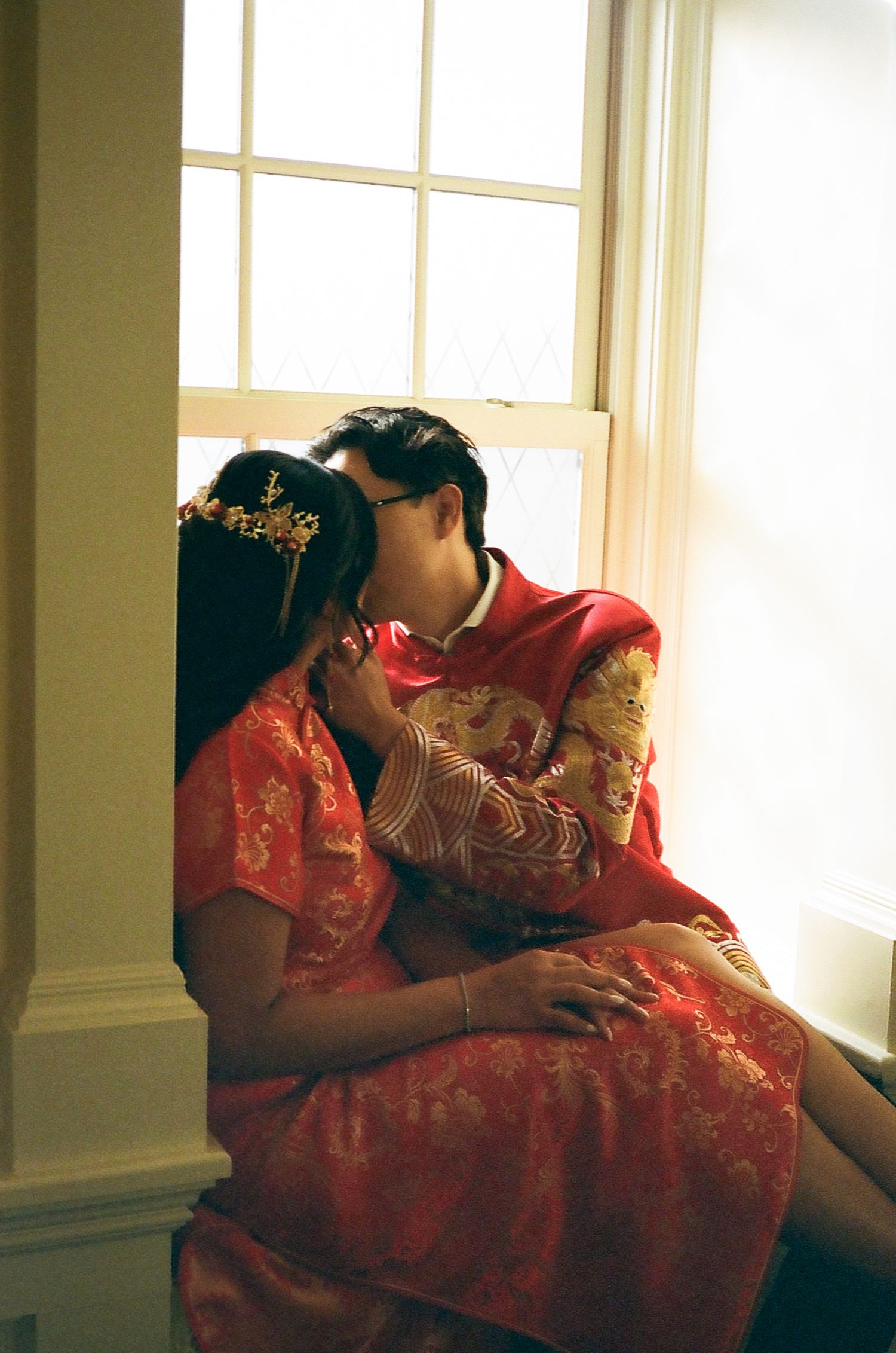 A person wearing a traditional red Chinese qipao dress sits by a window in soft natural light.