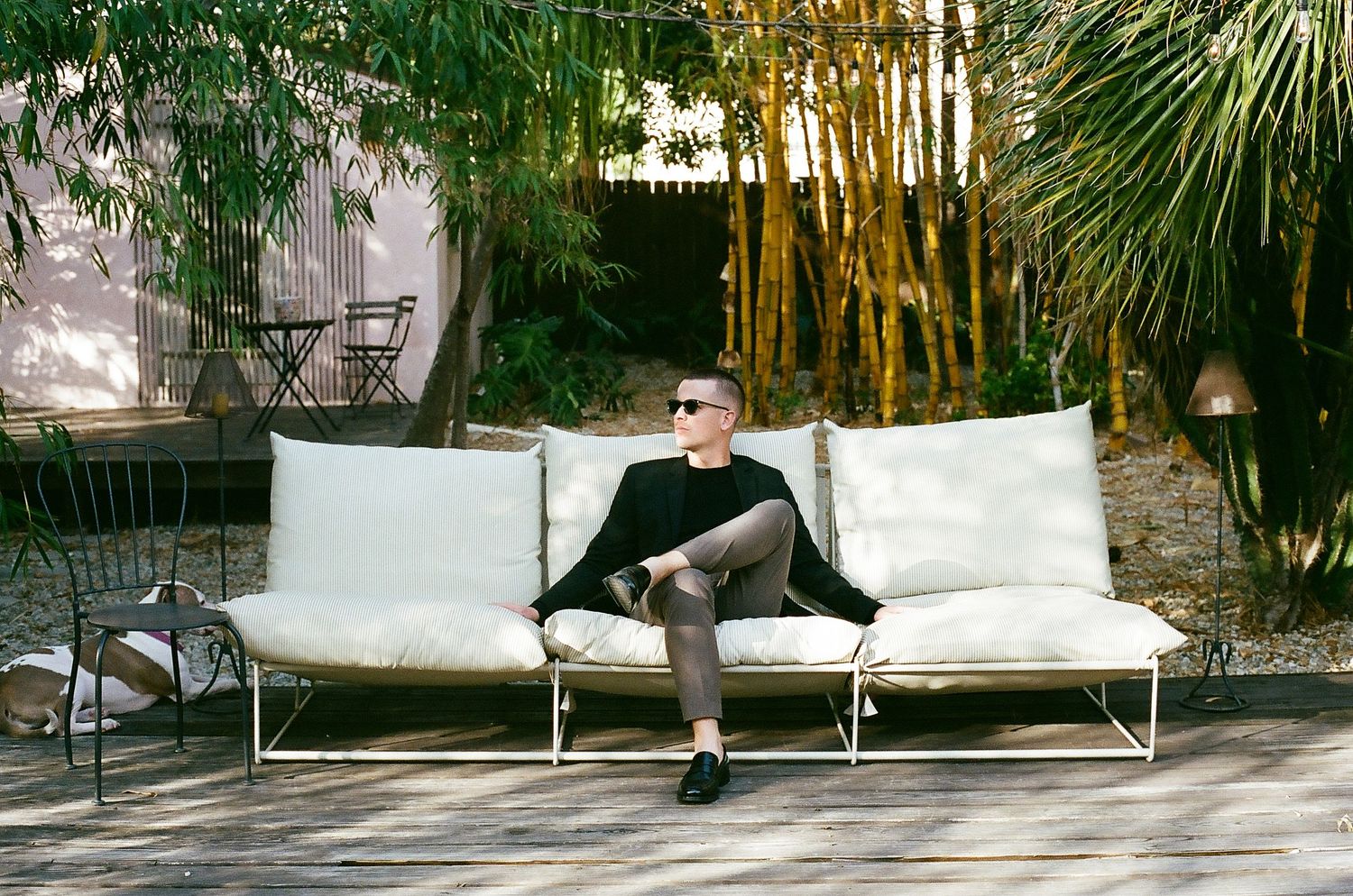 A sequence of black and white photos showing someone lounging on an outdoor patio sofa in a tropical garden setting.