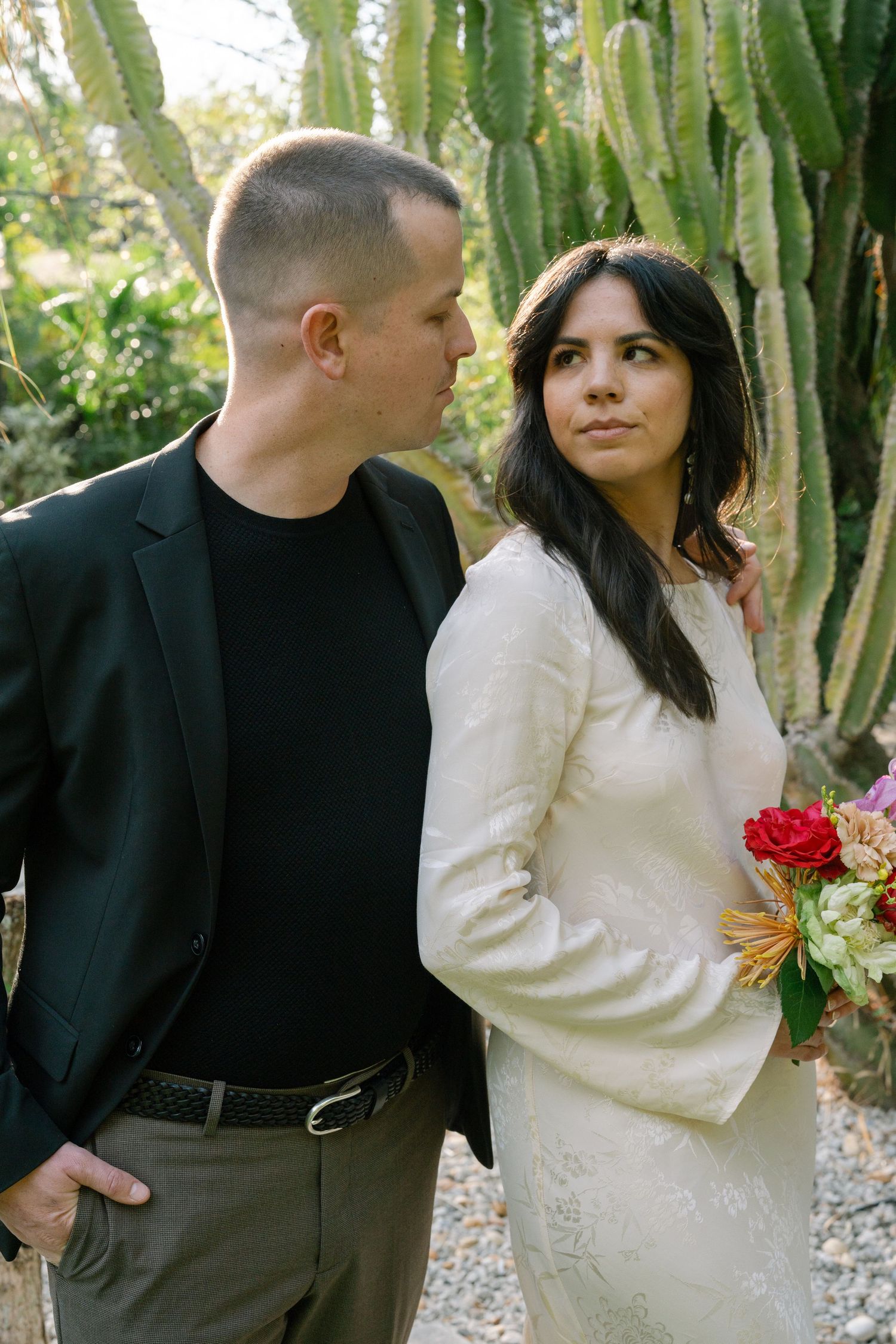A romantic couple shares intimate moments in a lush garden setting with tall cacti.