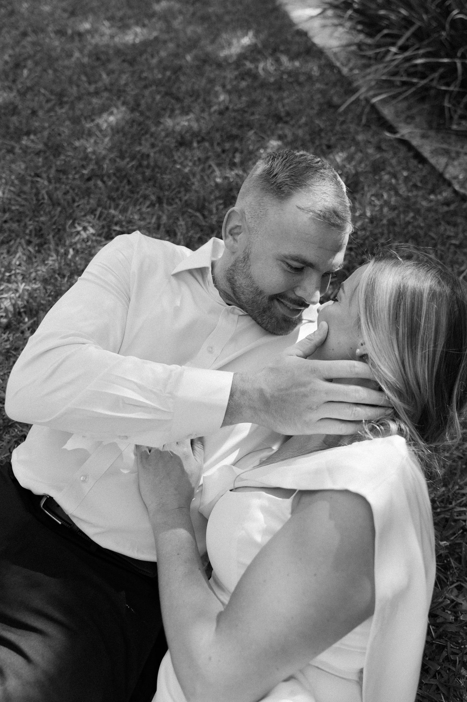 Intimate black and white photos capturing romantic moments between couple on grass in outdoor setting.