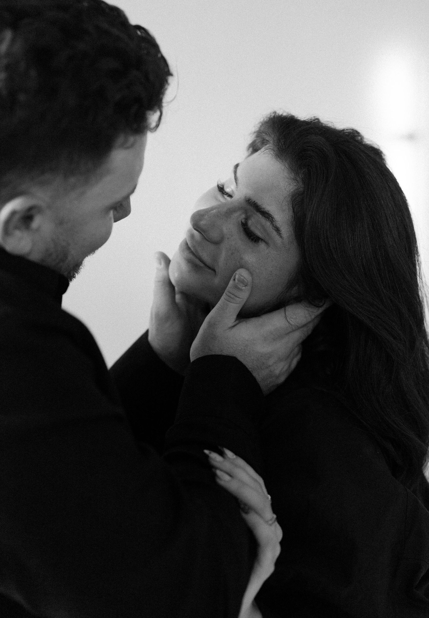 Intimate black and white portrait of a couple in an affectionate moment, both wearing dark clothing.