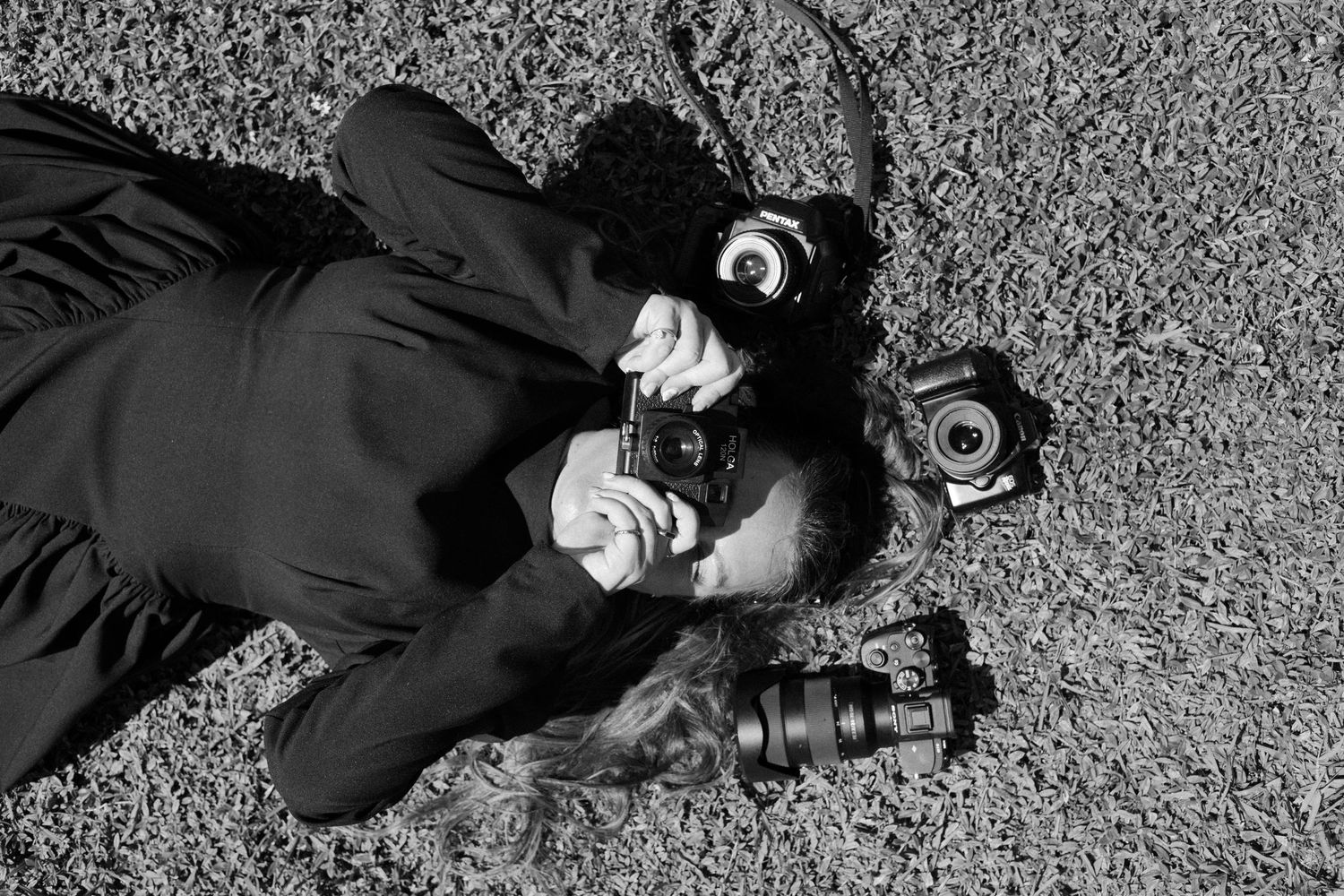 A person wearing goggles lies on the ground and takes a close-up photograph with a camera in black and white.