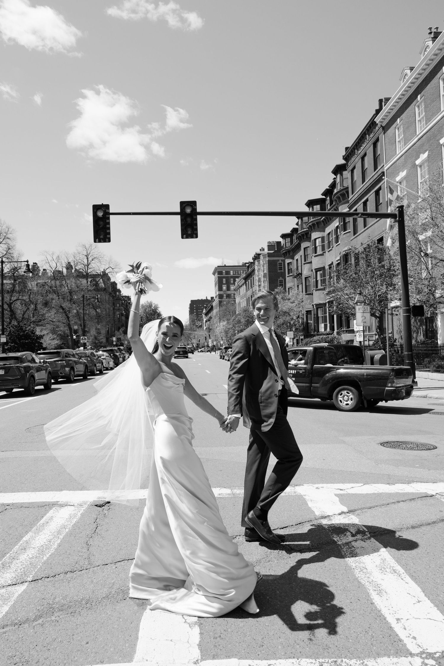 Black and white photo of bride and groom holding hands crossing a city street intersection on their wedding day.