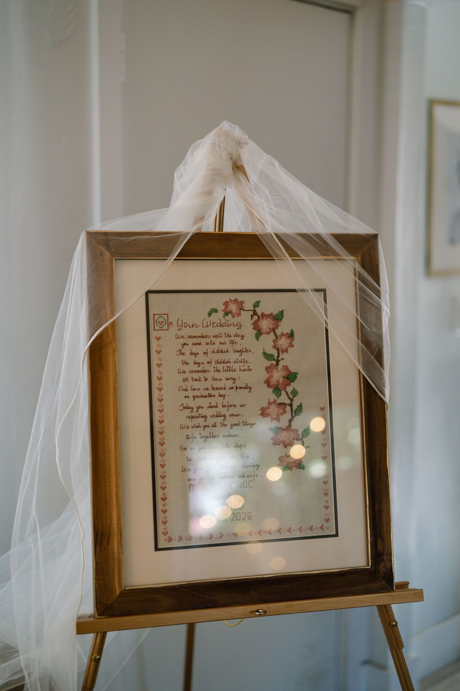 Framed wedding poem with floral illustrations displayed on a gold easel, adorned with flowing white tulle fabric.