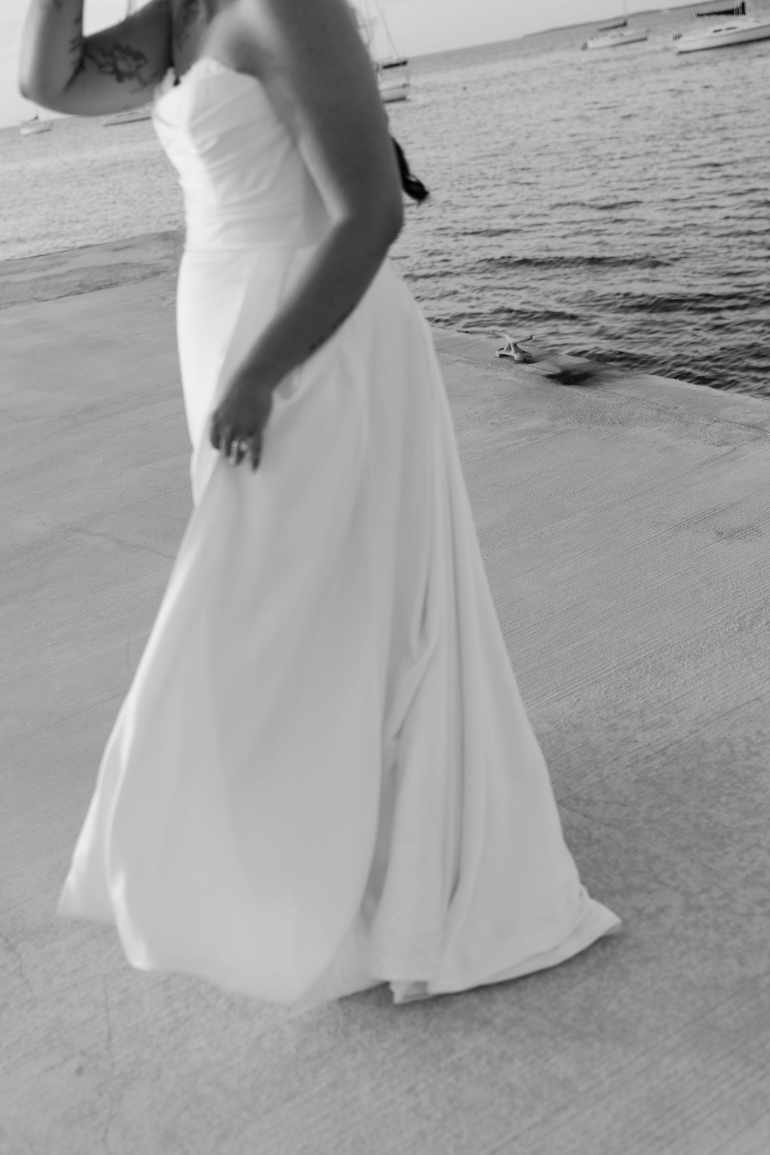 A woman in a white wedding dress stands on a beach with the ocean in the background.