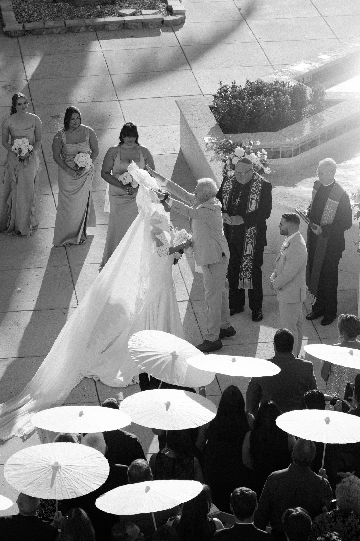 Black and white photo of wedding guests holding white paper parasols during an outdoor ceremony.