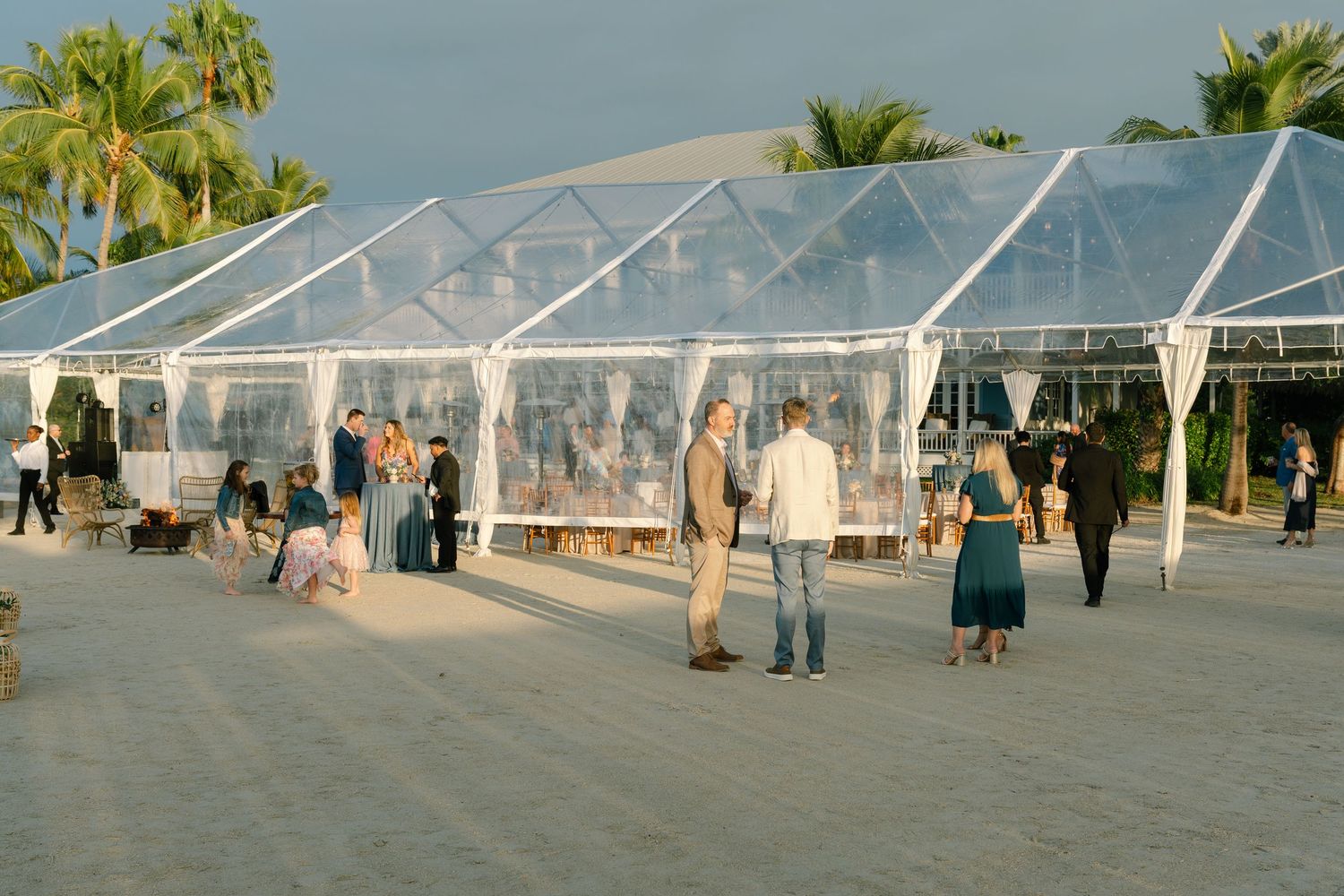Clear tent reception setup on the beach with palm trees and ocean views.