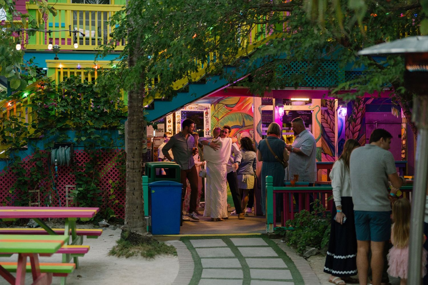 Colorful outdoor dining area with string lights and umbrellas creating a festive garden atmosphere.