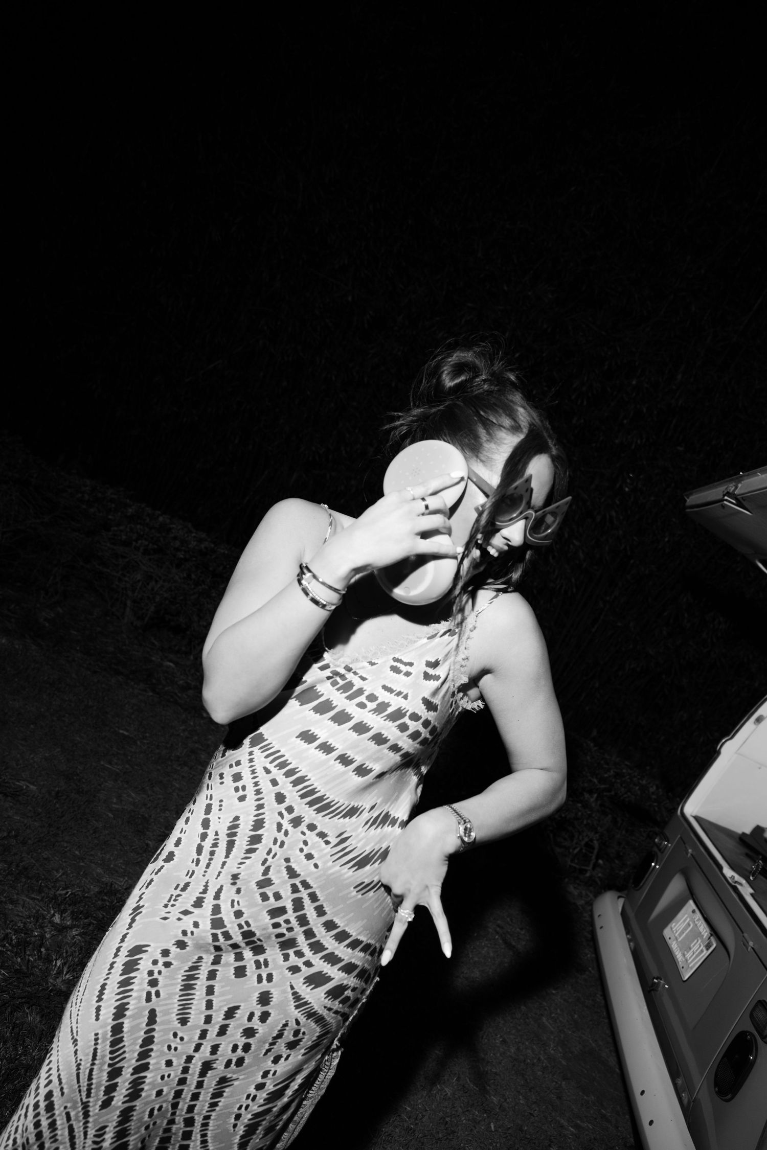 Black and white photo of woman in patterned dress dancing outdoors at night wedding reception.