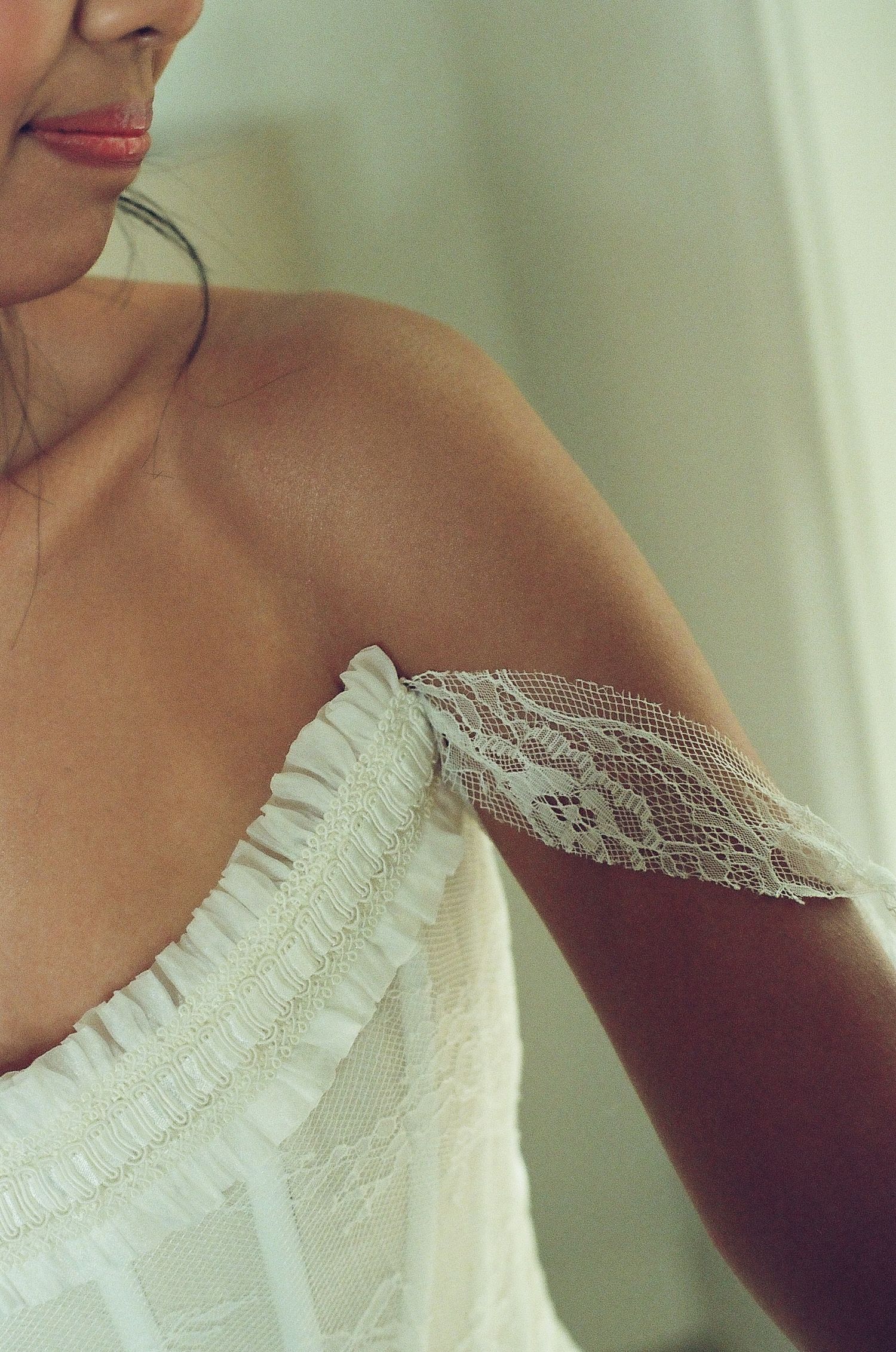 Close-up of a woman in a white lace off-shoulder bridal dress with delicate ruffle and lace sleeve detail.