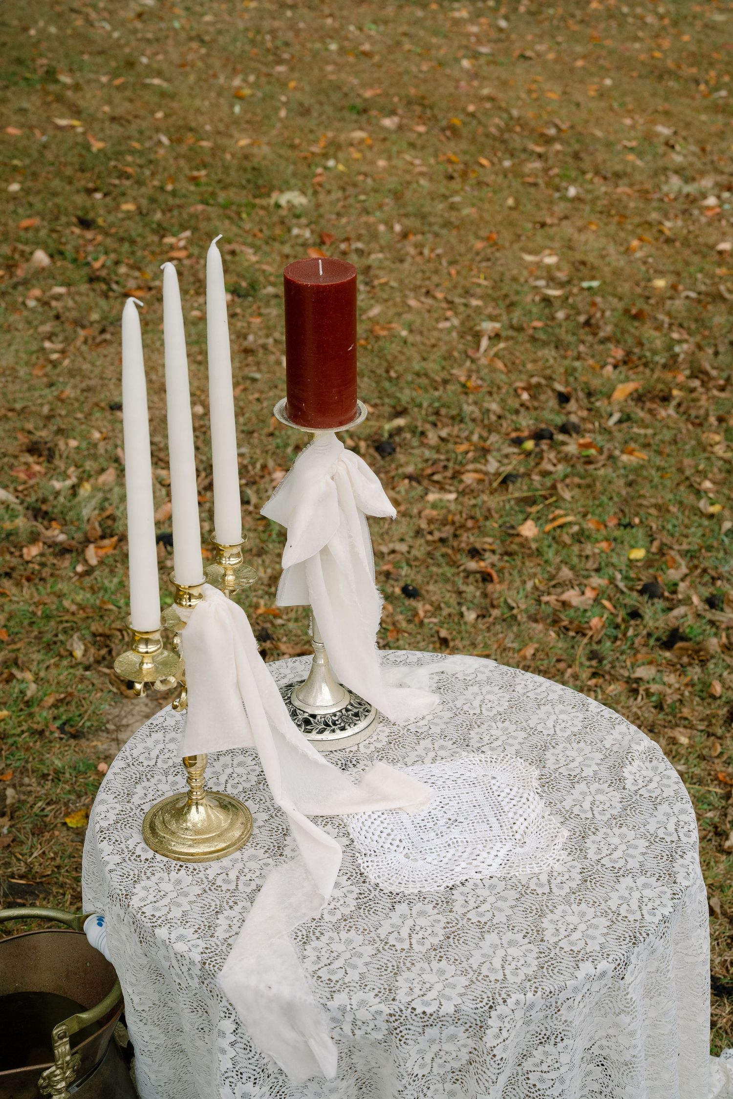 Elegant candle arrangement with white and red taper candles on lace tablecloth with scattered autumn leaves in background.