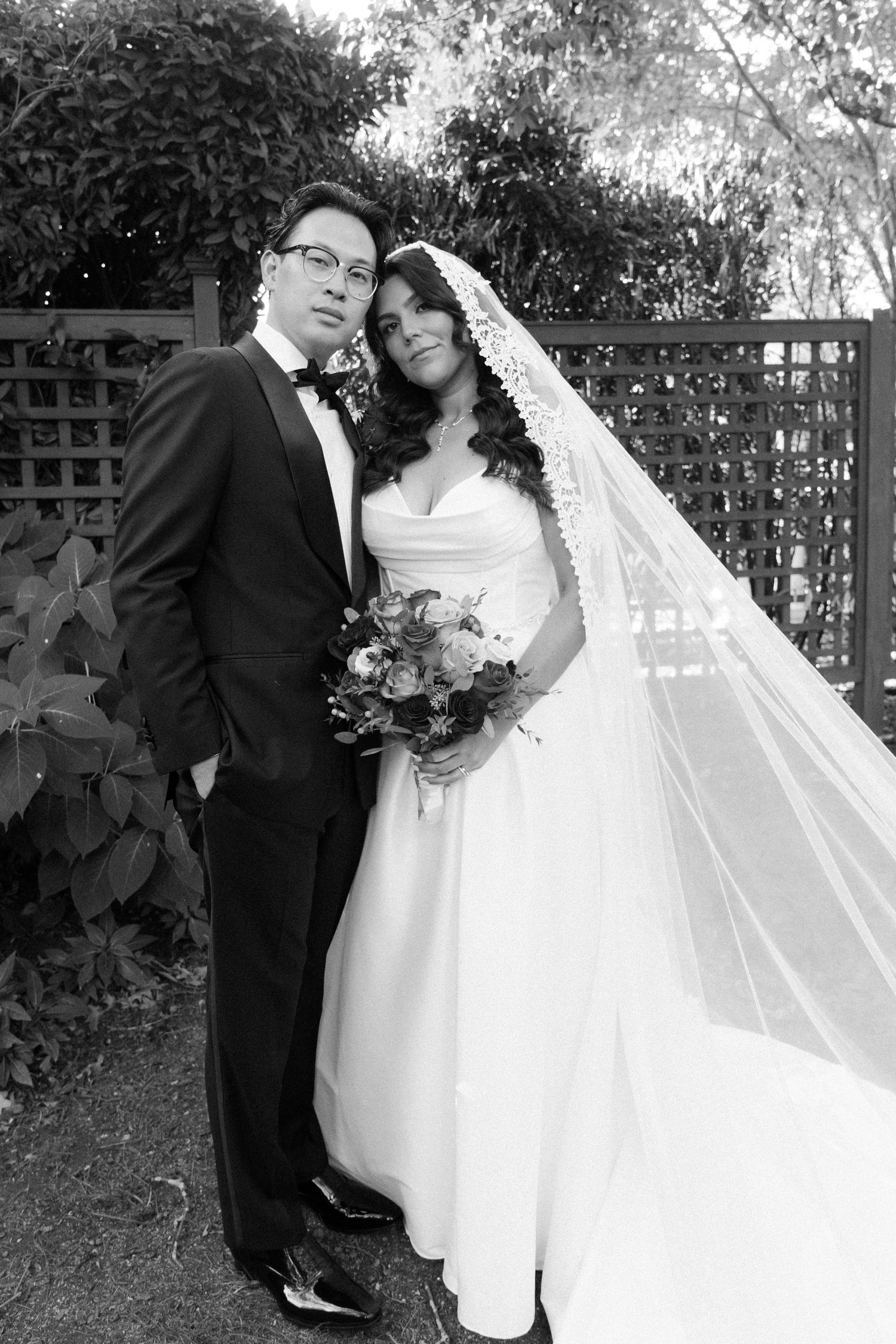 Black and white romantic wedding portraits captured in a garden setting with dramatic lighting.
