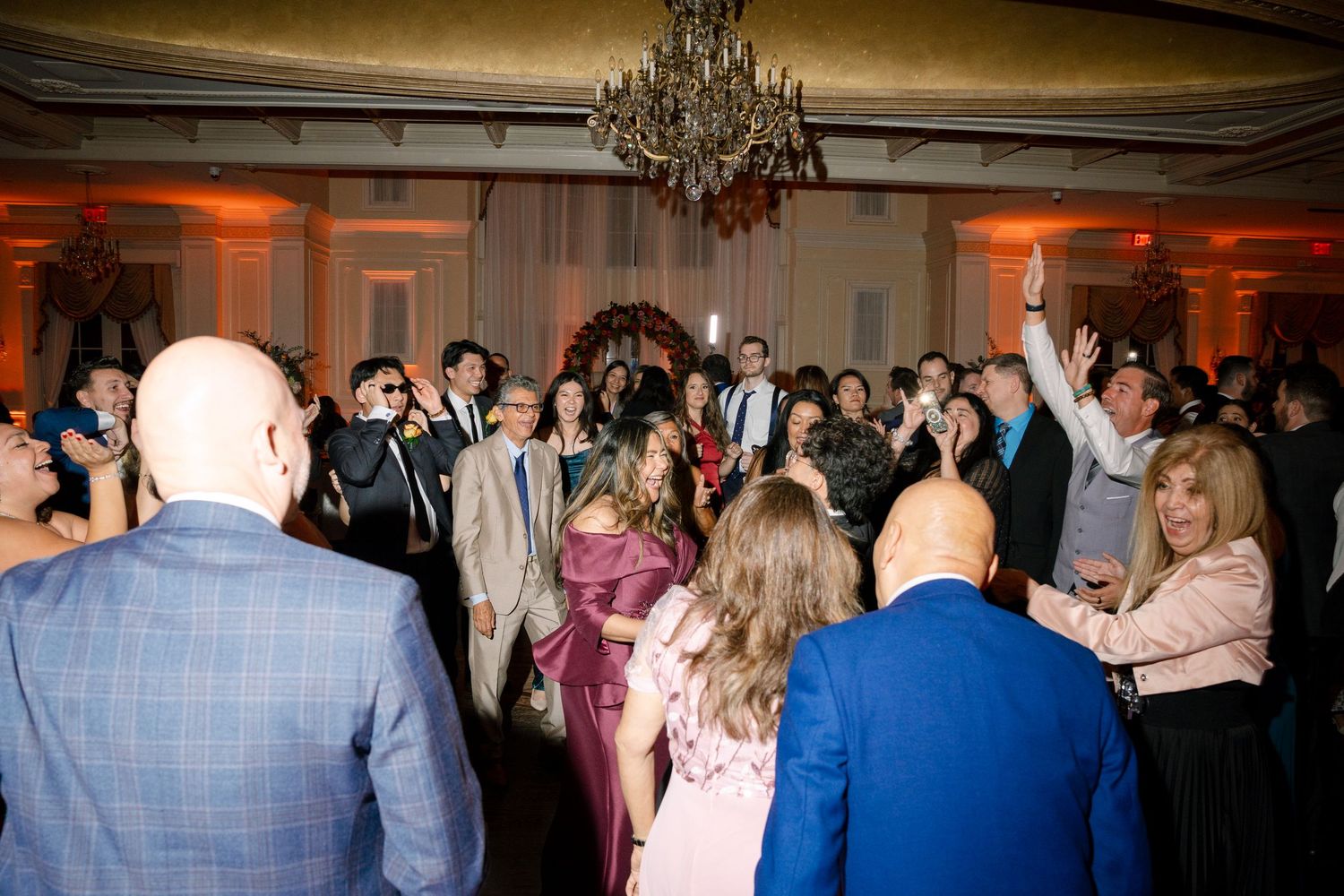 Dimly lit ballroom filled with wedding guests dancing at an evening celebration.