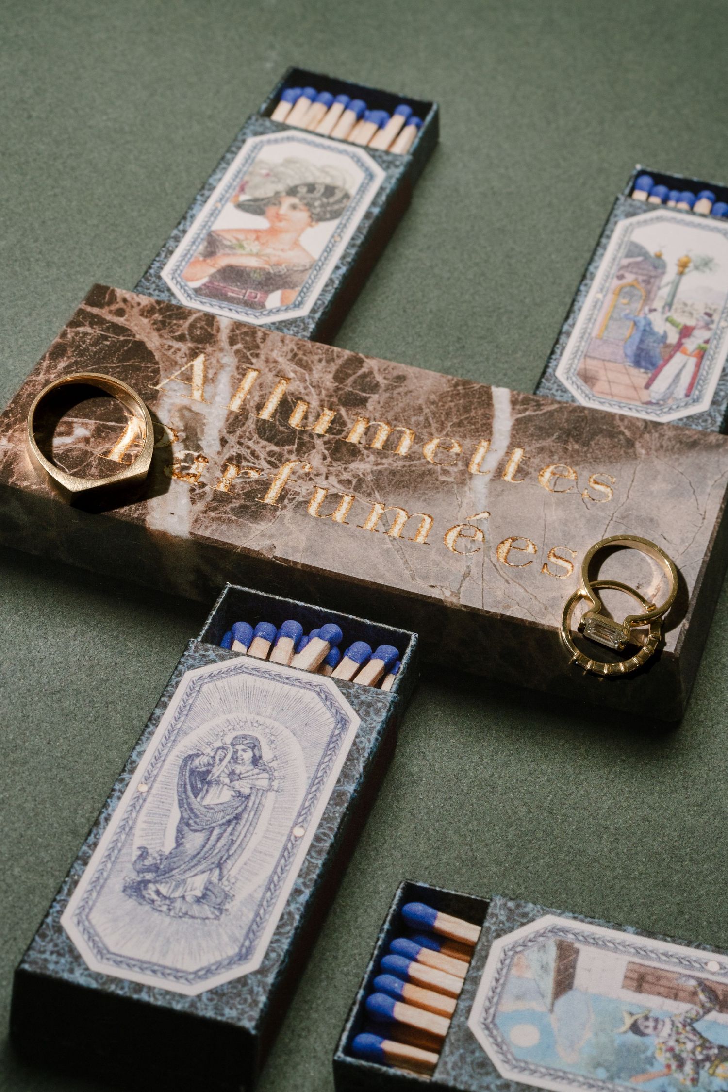 Close-up of vintage matches and matchboxes with decorative blue designs arranged in a cross pattern on a green surface.