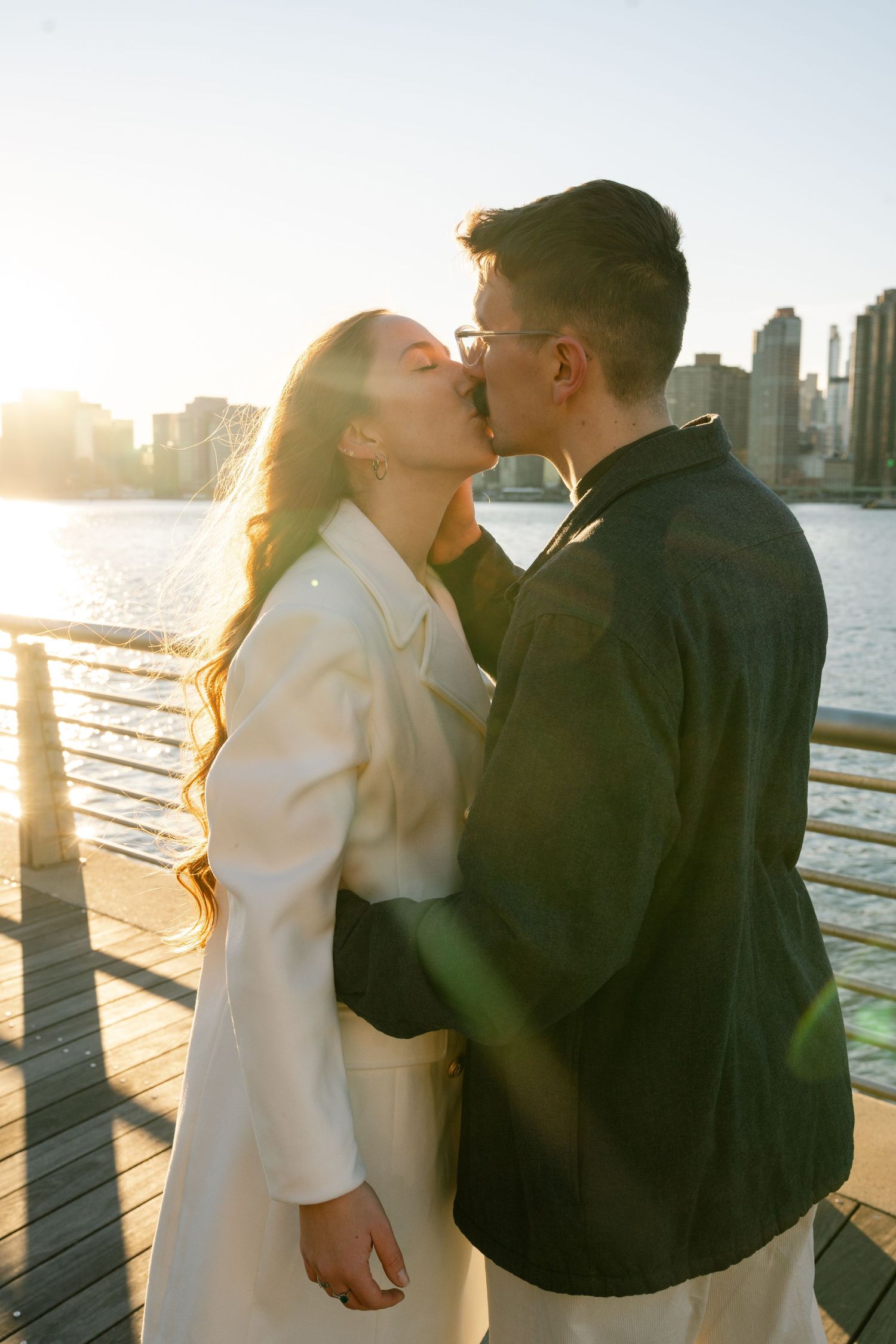 A tender moment between a couple sharing a kiss at sunset with the city skyline behind them.