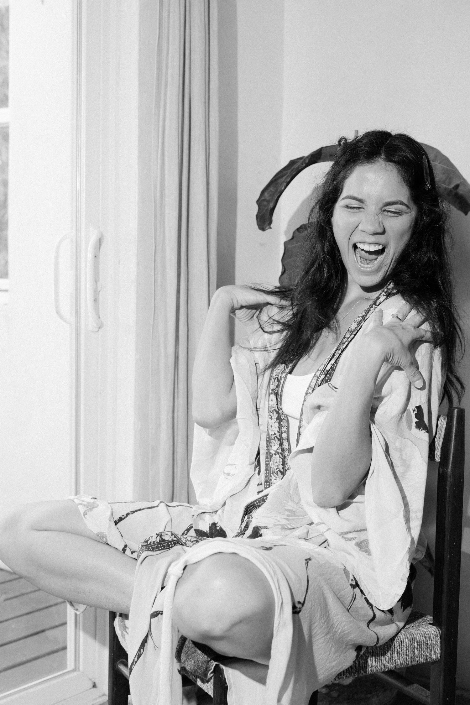 A candid black and white photo showing joyful laughter while sitting by a window.