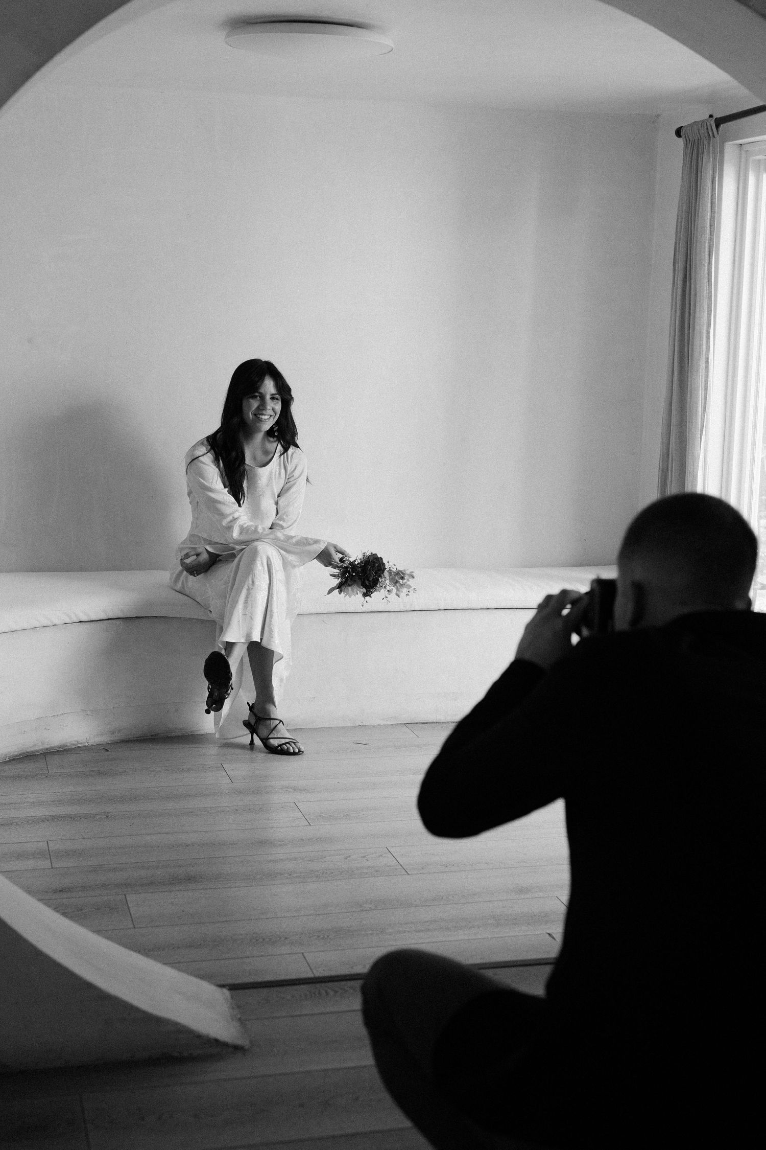 A photography session in progress showing dramatic black and white poses in a minimalist white studio space.
