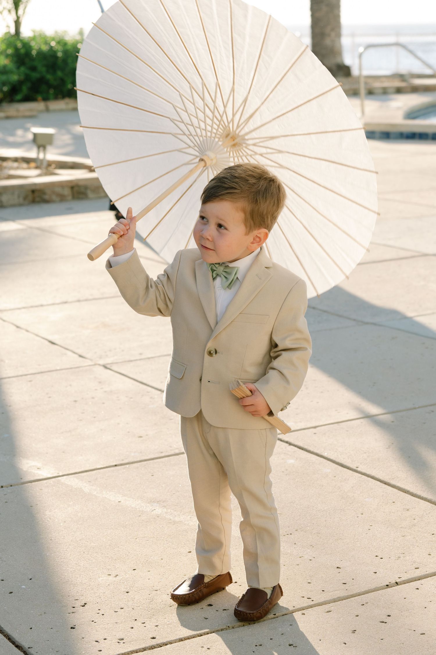 Small child in beige suit plays with white parasol outdoors.