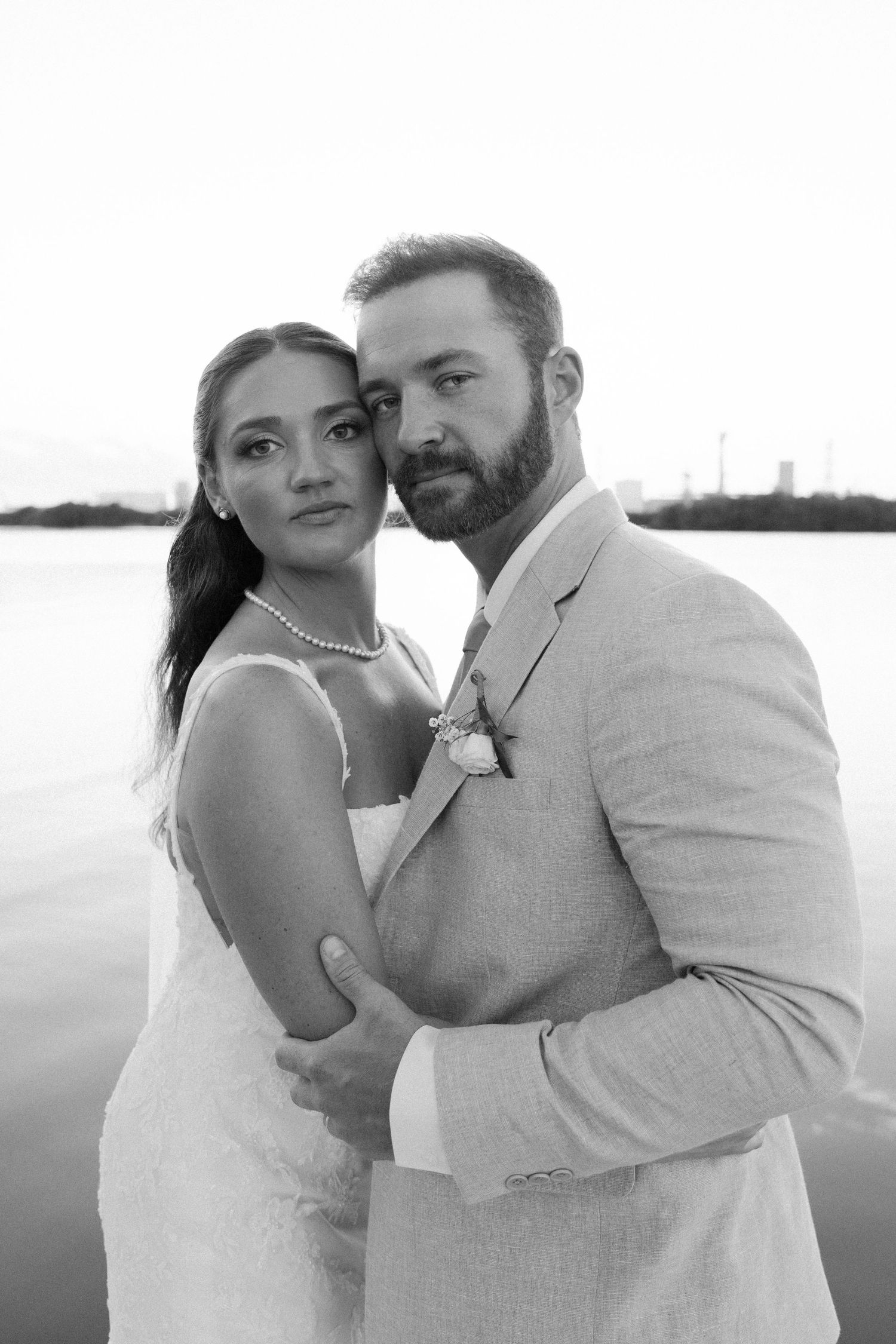 A series of romantic black and white wedding photos showing a couple embracing by the water at sunset.