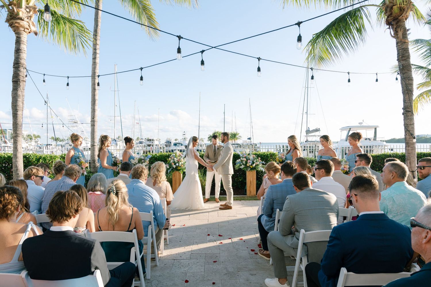 A panoramic view of a beachfront wedding ceremony setup with palm trees and string lights.