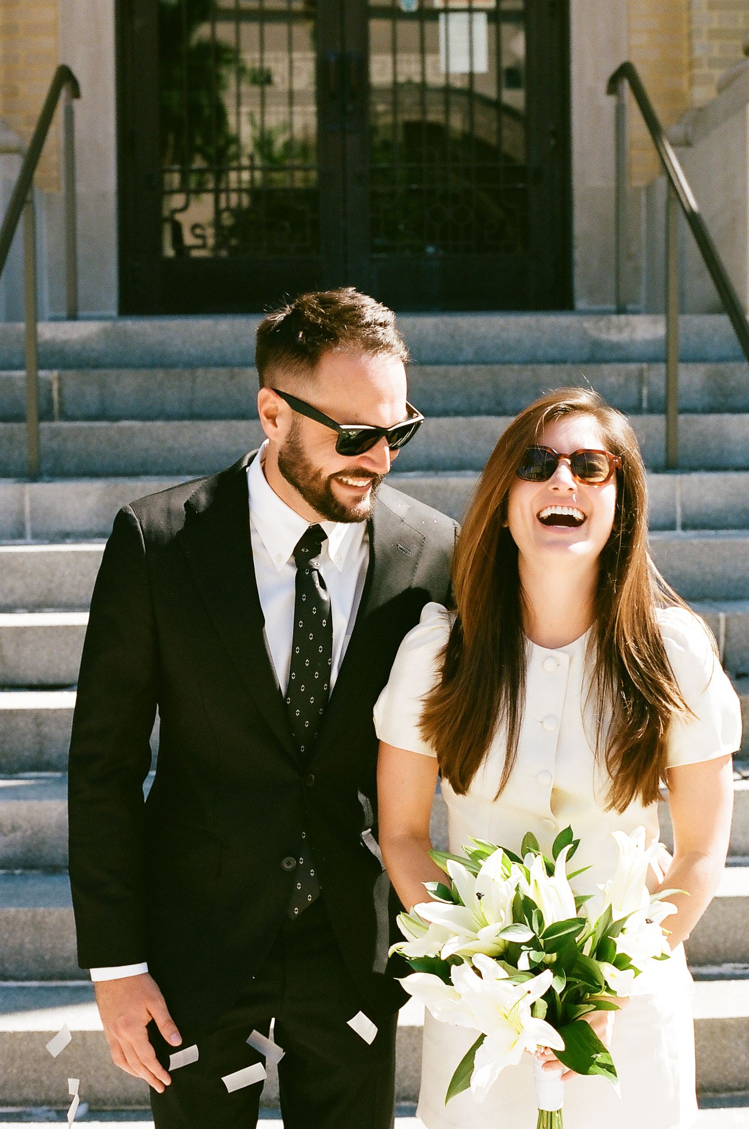 Stylish couple sharing laughter while holding white lilies outdoors.