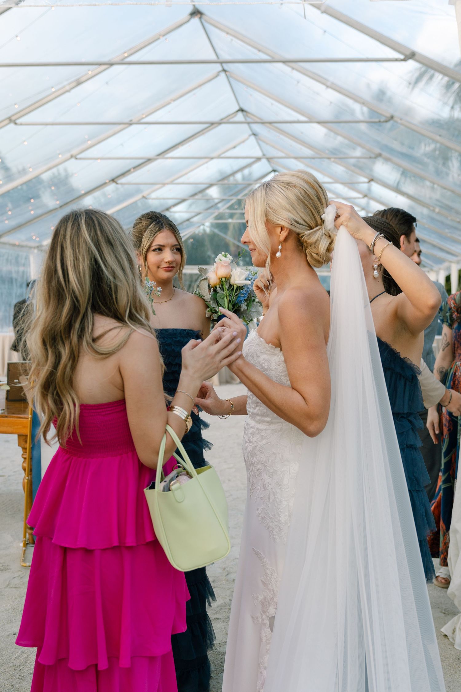 Wedding guests in pink bridesmaid dresses share emotional embraces with the bride in a clear tent reception venue.