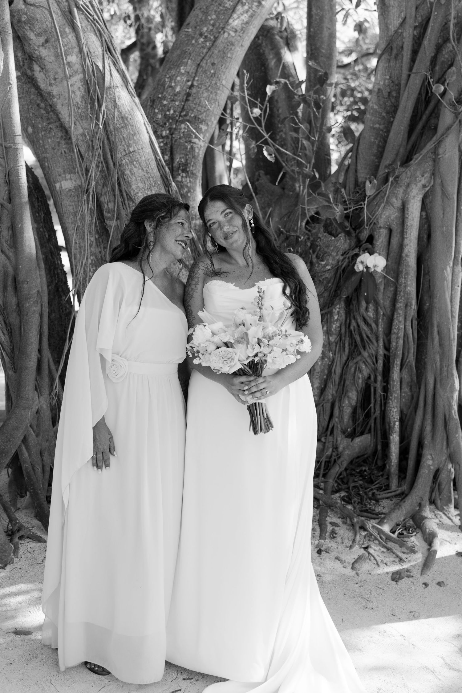 Two women in white dresses standing together in a lush, forested area.