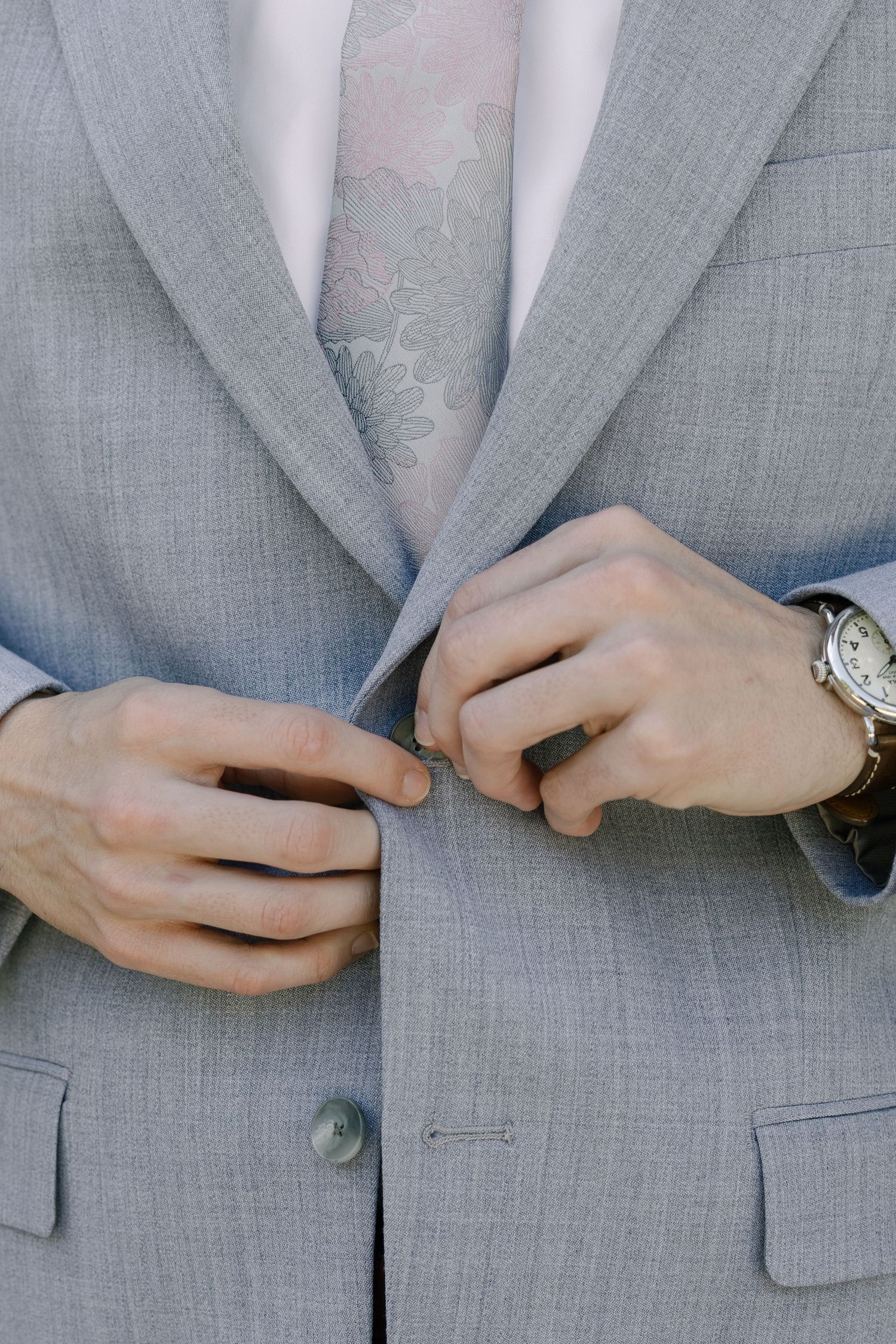 A person's hands buttoning up a gray suit jacket.
