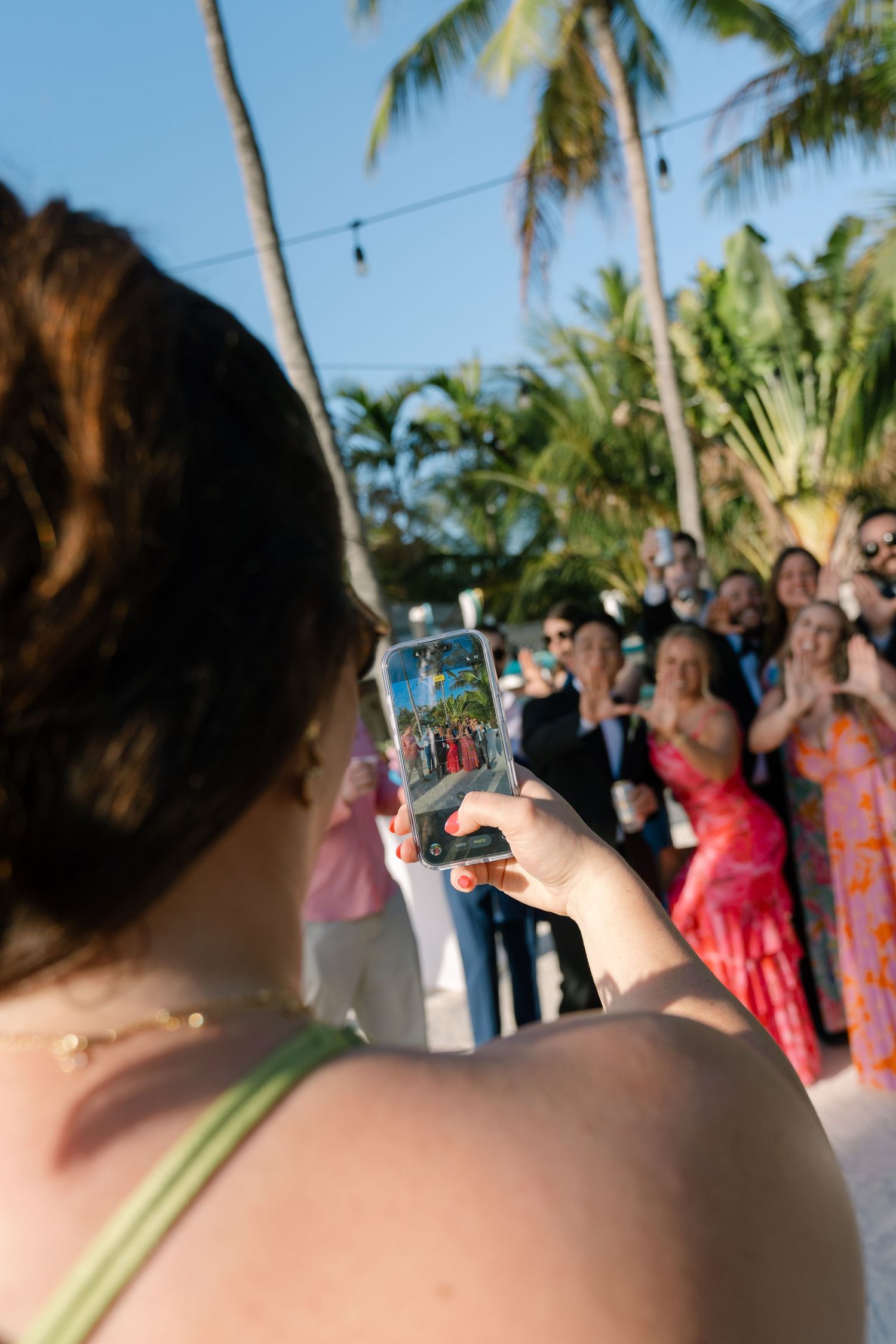 A person holds a smartphone and takes a photo of a group of people dressed in colorful, formal attire at an outdoor event.