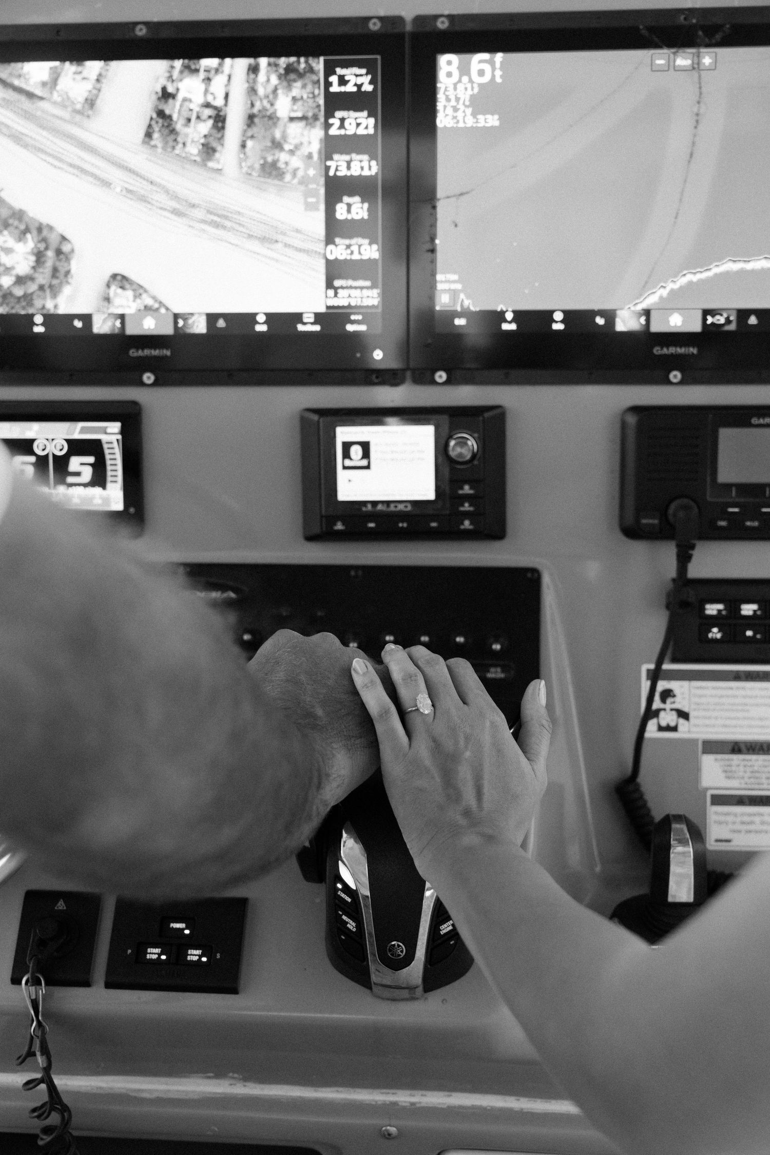 Multiple black and white security camera monitors display surveillance footage while hands interact with control panels.