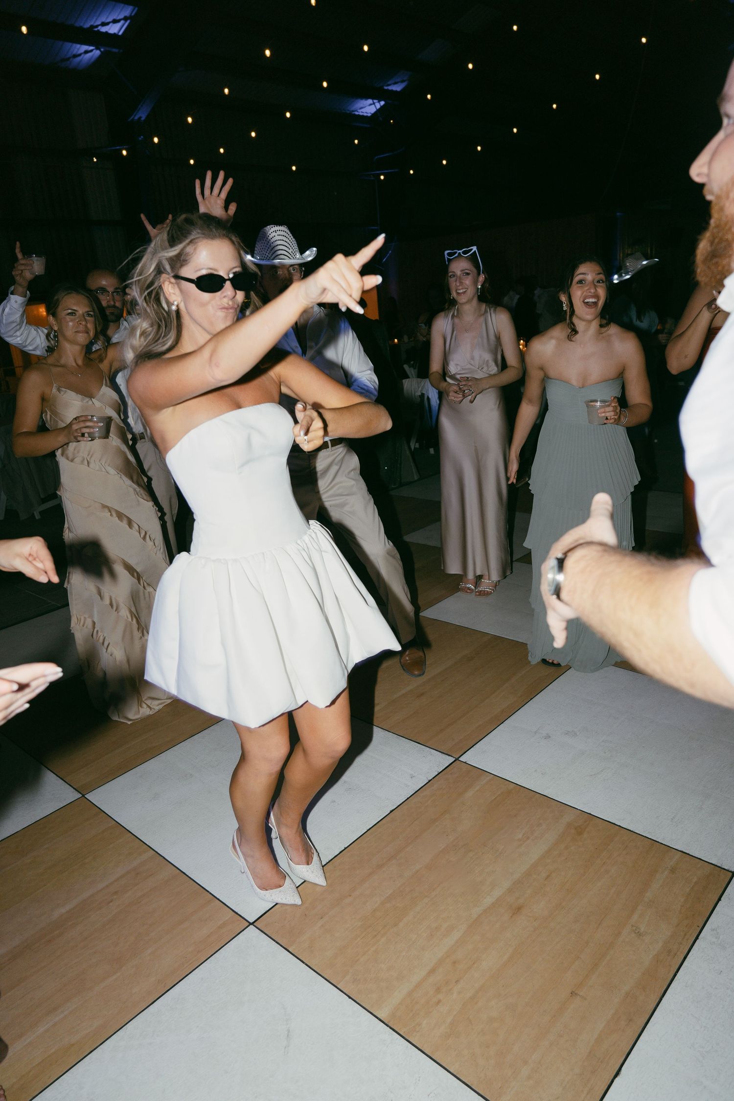 Wedding party dancing and celebrating on a wooden dance floor at night during reception festivities.