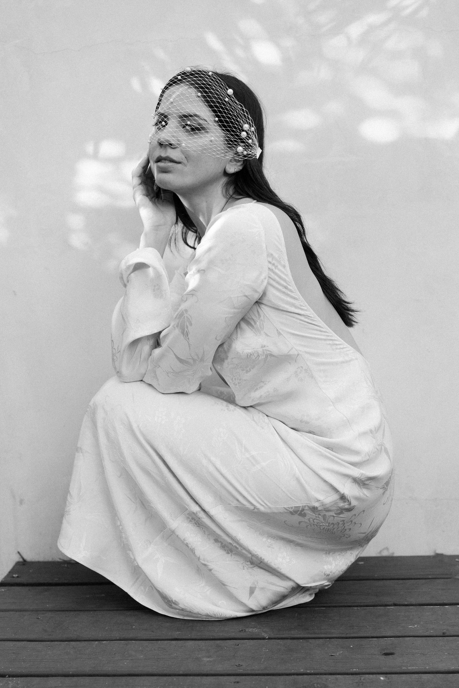 A dreamy black and white portrait showing a figure in white dress seated outdoors.