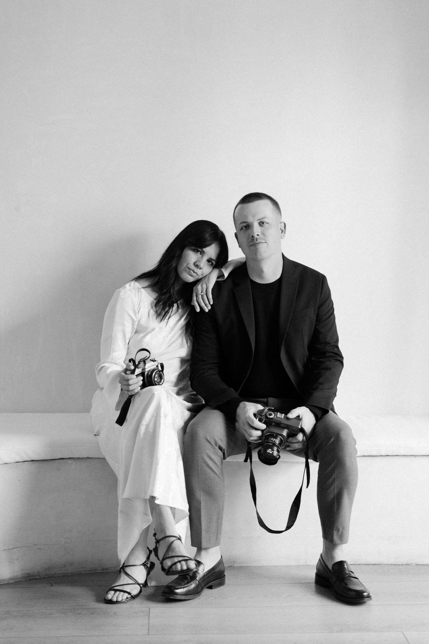 Black and white photo series showing two people with cameras in a minimalist setting.